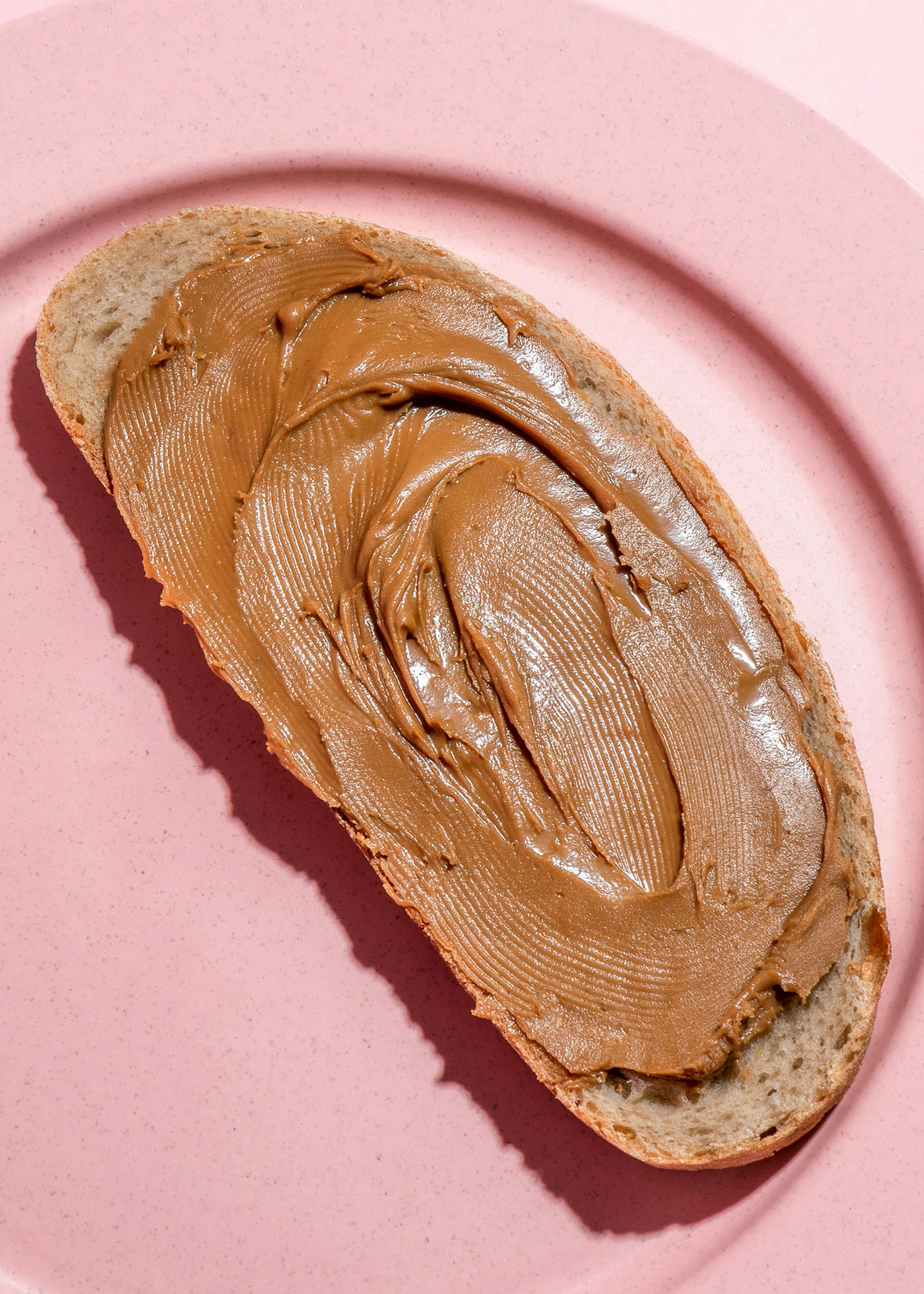 a piece of bread with peanut butter on it on a pink plate