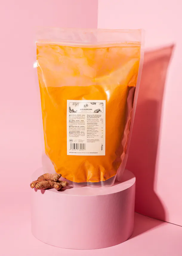 un sac de poudre de curcuma est posé sur un support rose