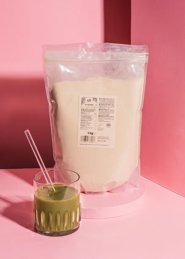 a glass of green smoothie next to a bag of powder