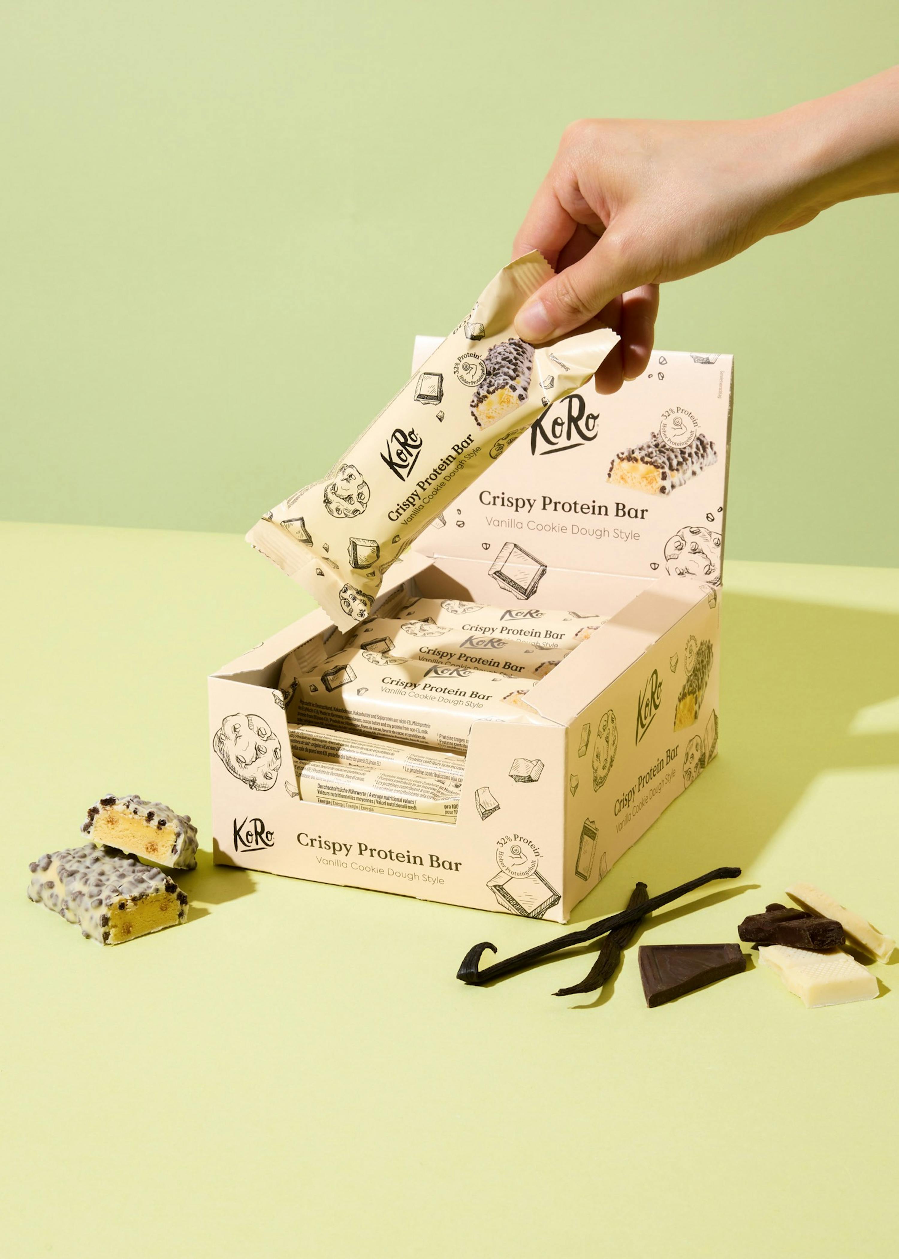 une personne tient une barre de protéines croustillante à côté d' une boîte