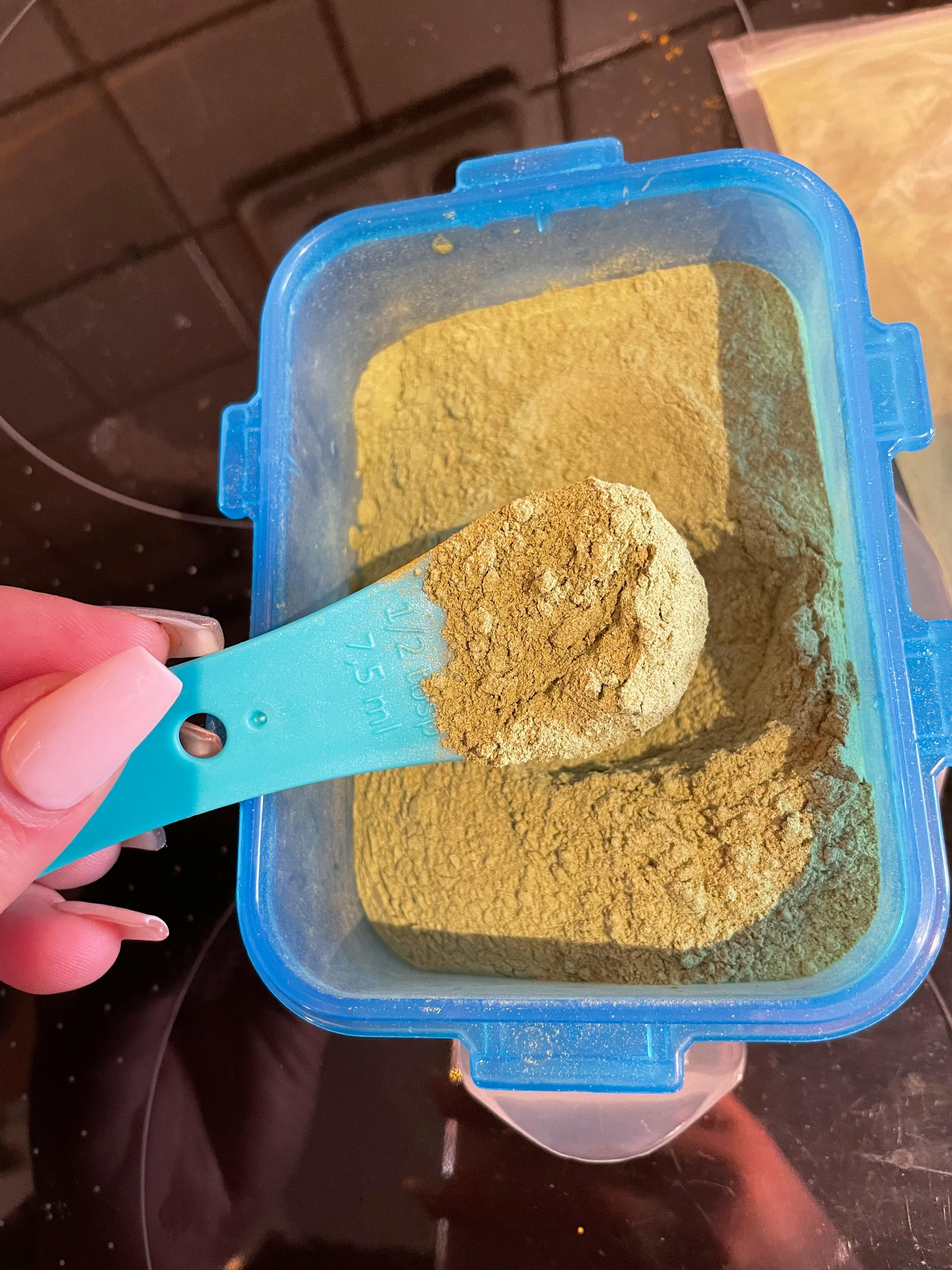 a blue measuring spoon is being used to measure a container of powder