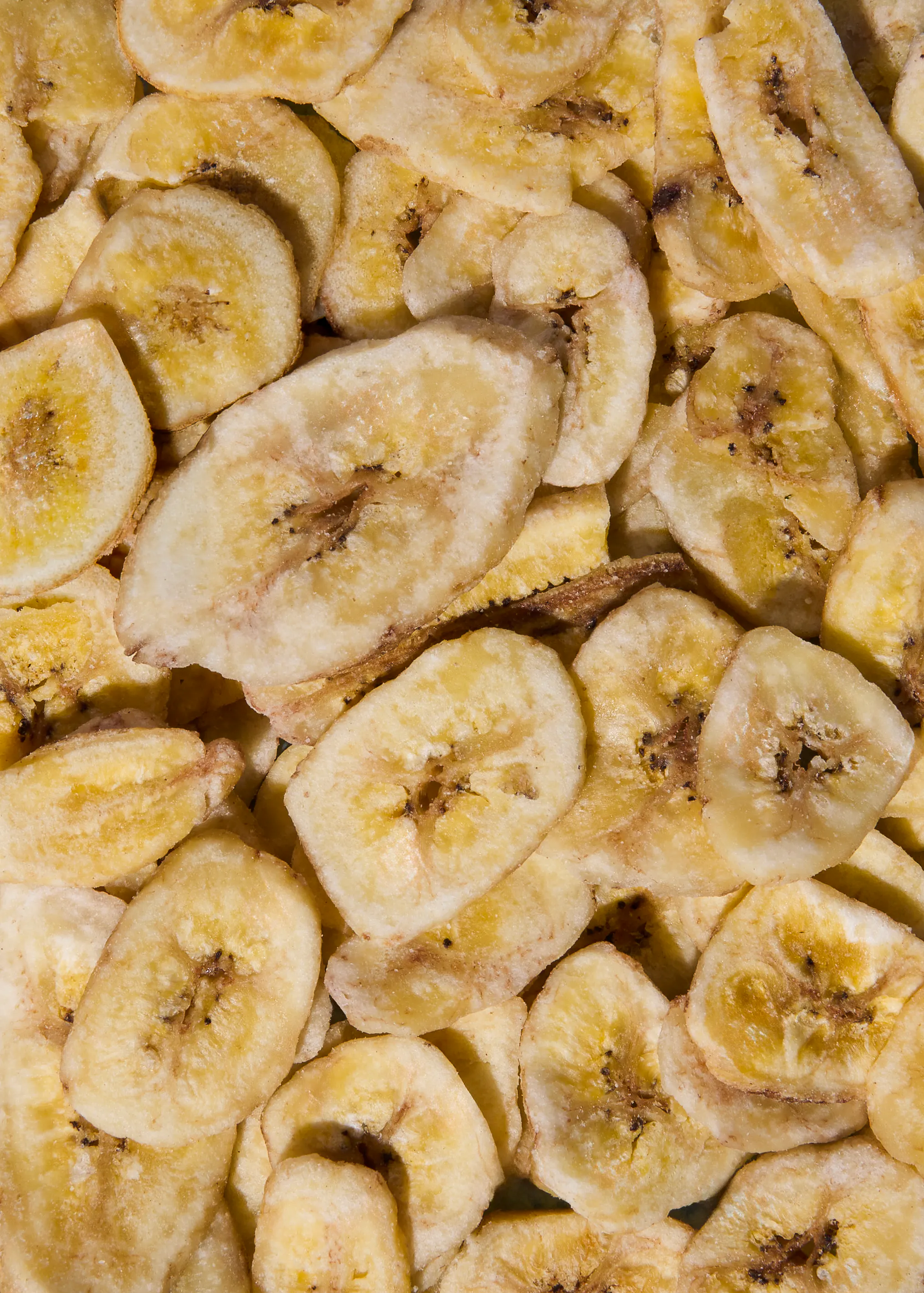 ein haufen getrockneter bananenscheiben, die hellgelb bis cremefarben sind und dunklere kerne aufweisen.