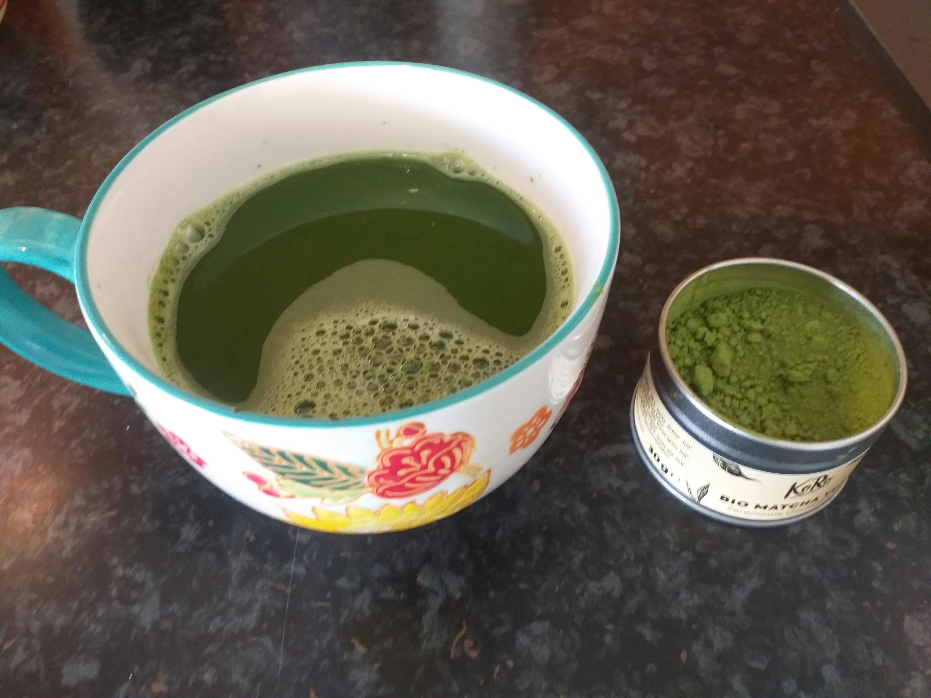 a can of matcha powder next to a cup of matcha