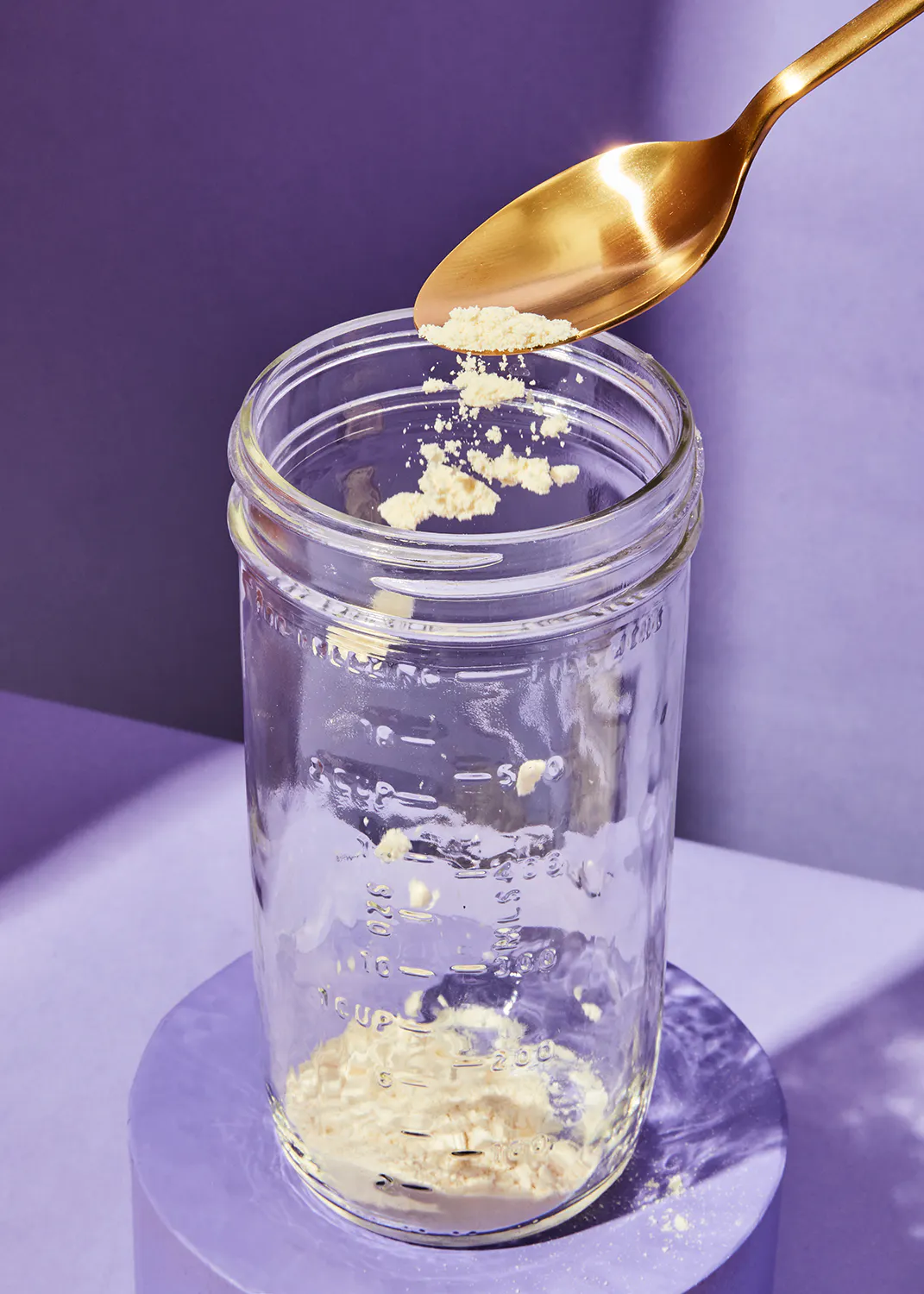 une cuillère est versée dans un bocal de verre rempli de poudre