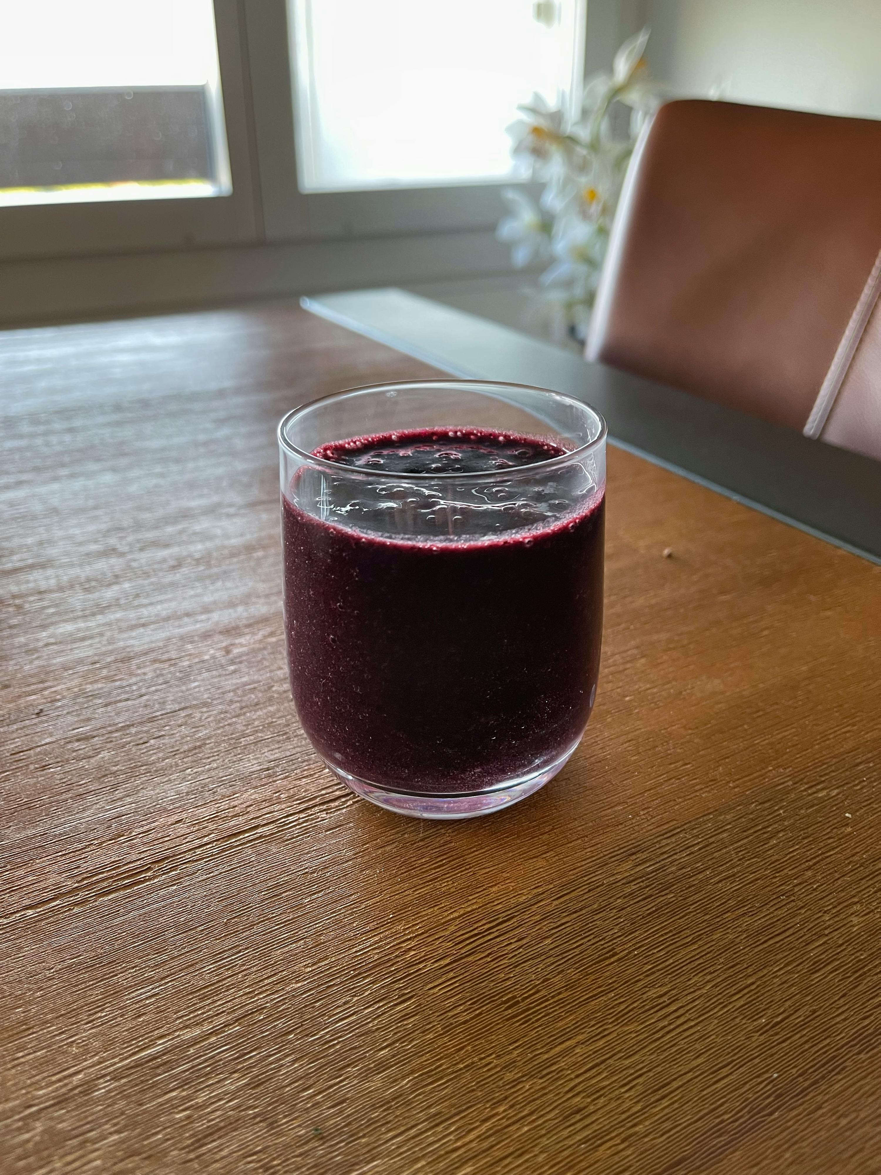 un verre rempli d' un liquide violet est posé sur une table en bois