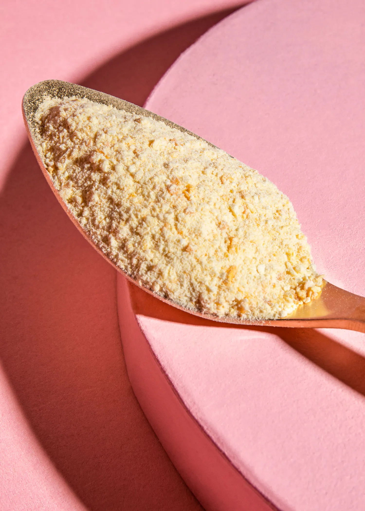 une cuillère remplie de poudre est sur une surface rose