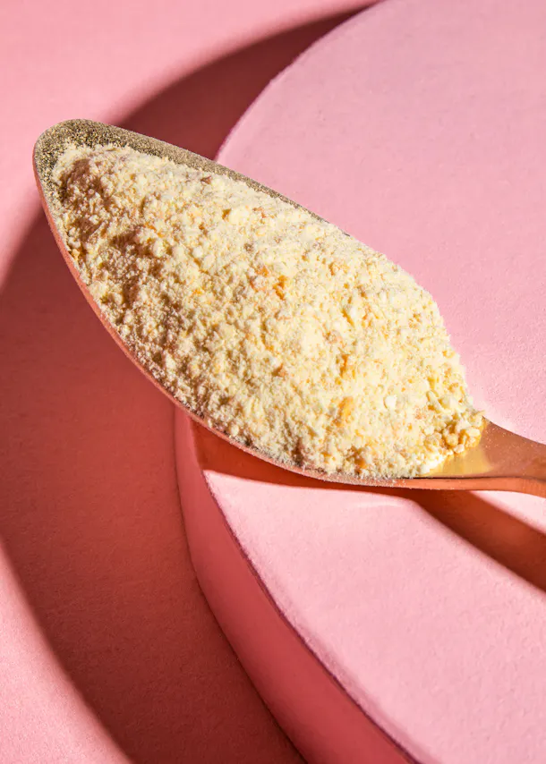 une cuillère remplie de poudre est sur une surface rose