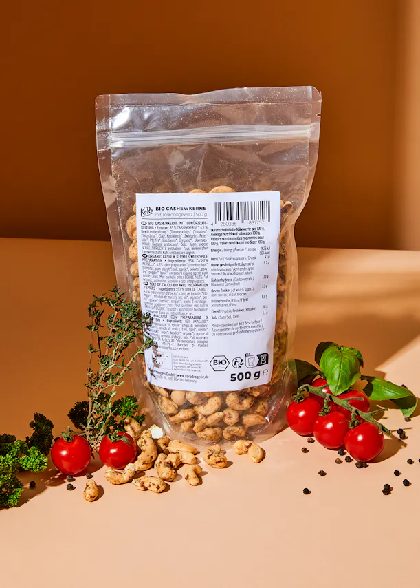 un sac de noix de cajou est assis sur une table avec des tomates et des herbes
