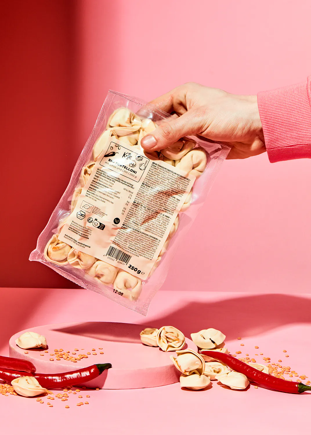 a person is holding a bag of tortellini on a pink background