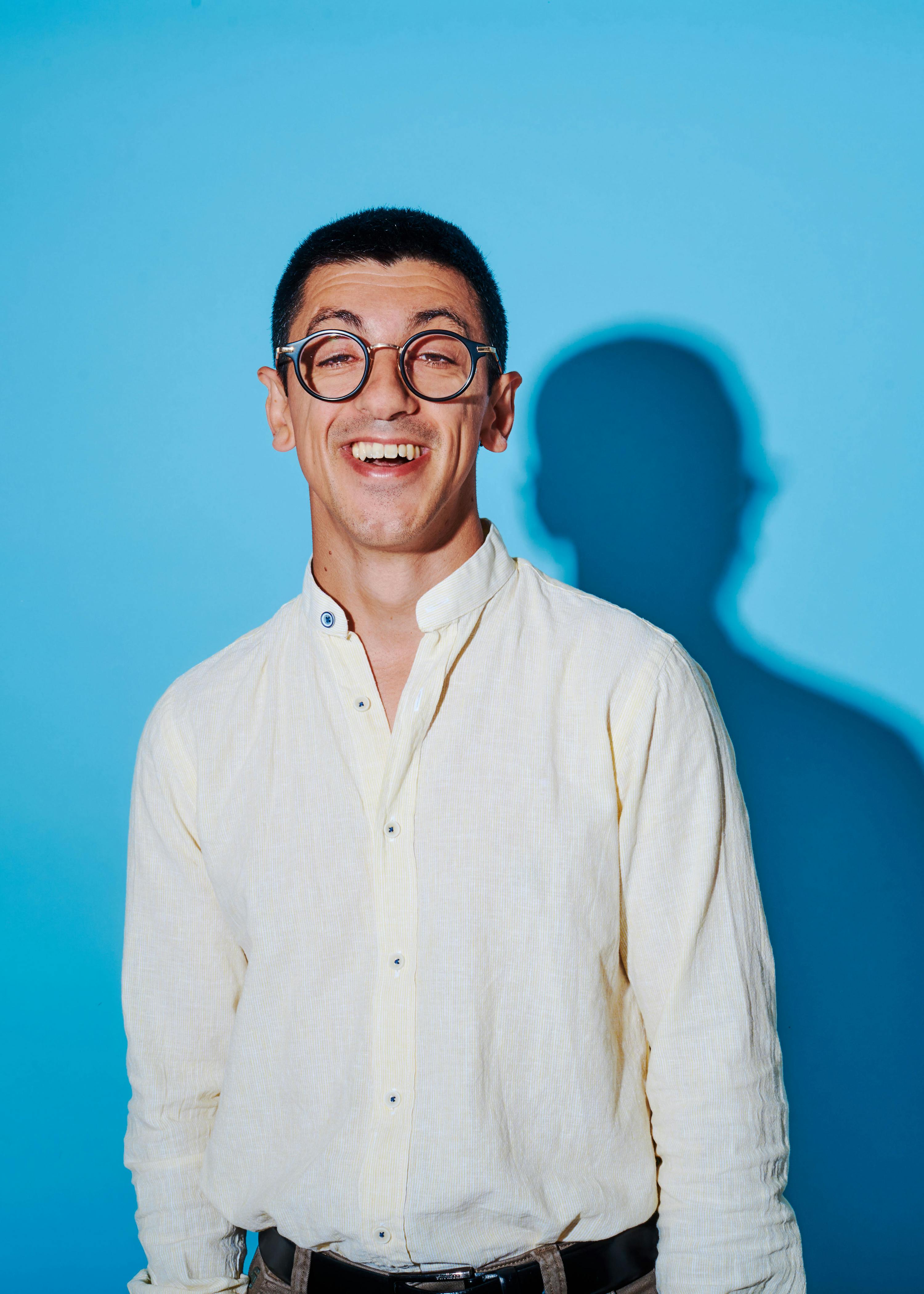 un homme portant des lunettes et une chemise blanche sourit