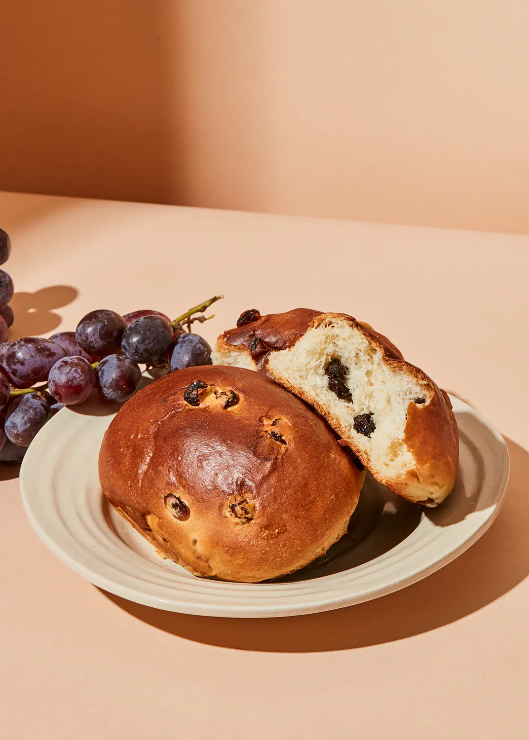 a bun with raisins on it is on a plate next to grapes