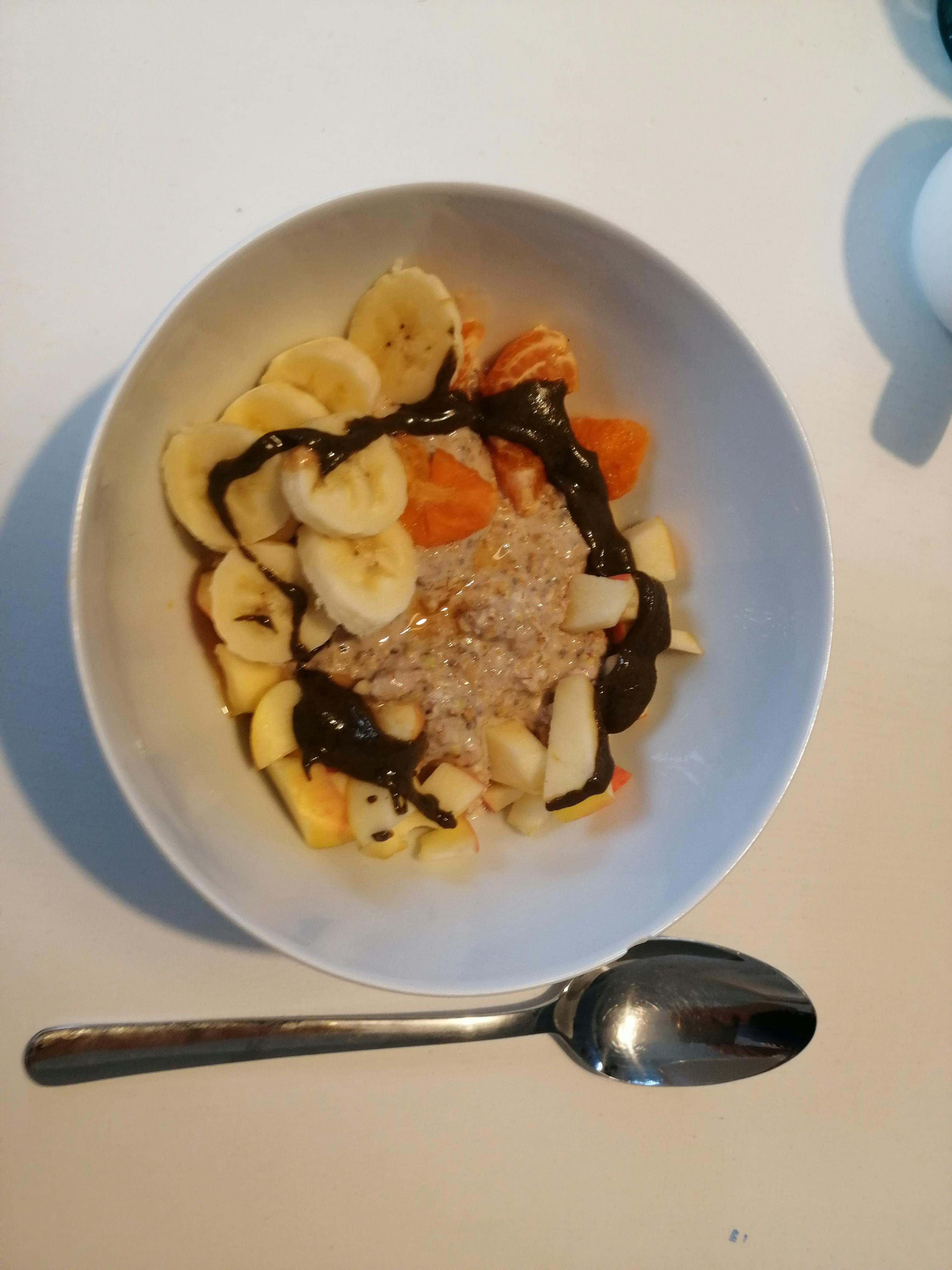 a bowl of oatmeal with bananas and chocolate sauce next to a spoon