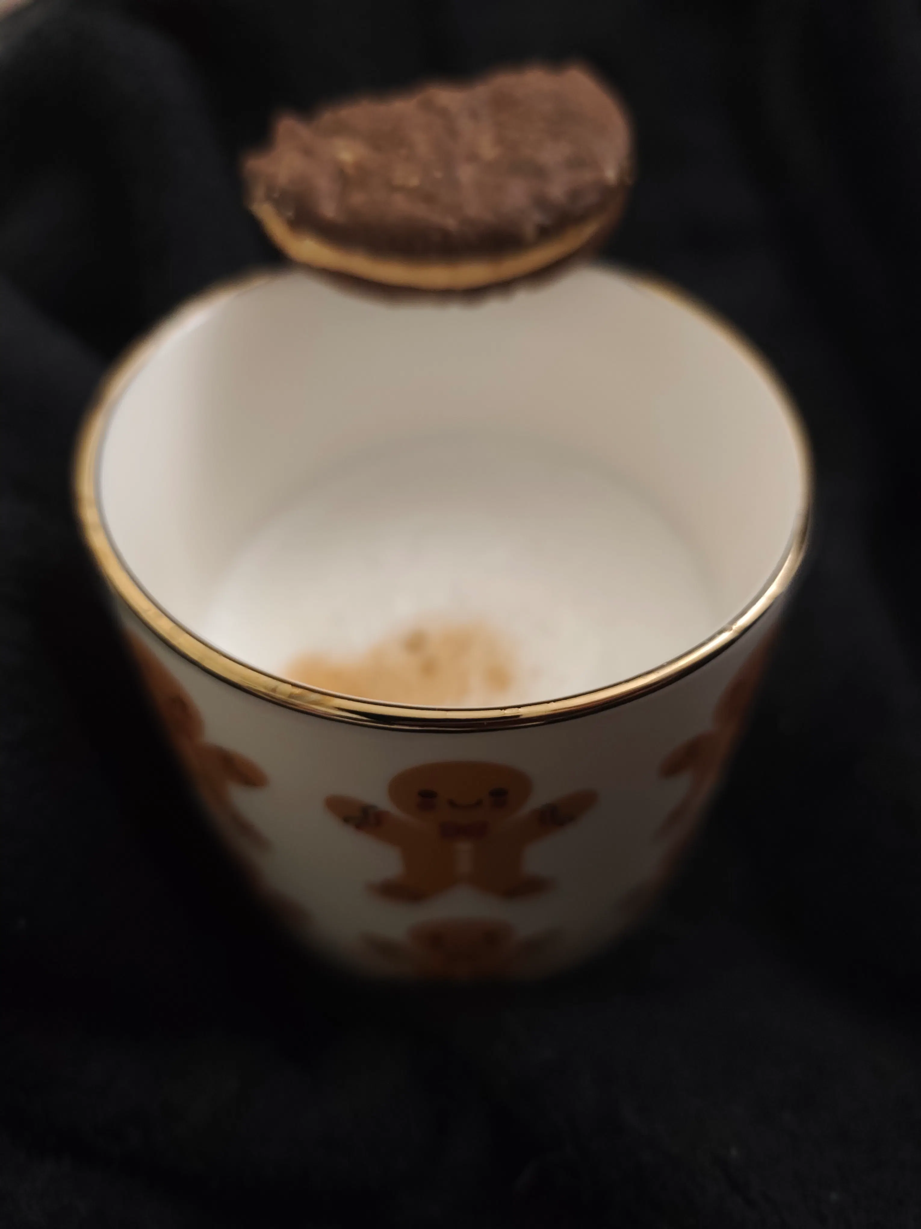 ein keks schwebt über einer weißen tasse mit lebkuchenmann-muster, die mit milch gefüllt ist.