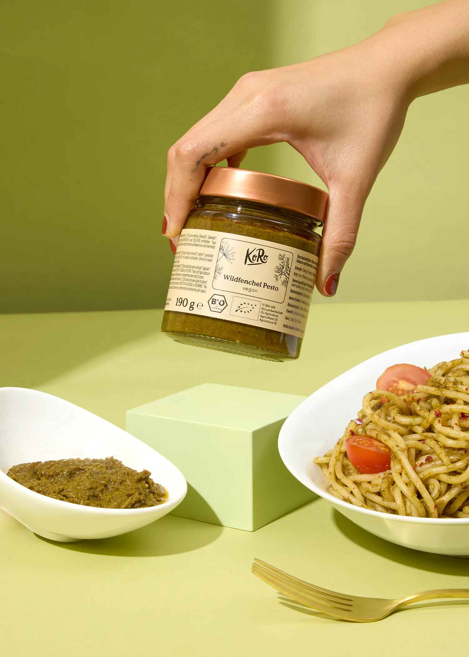 eine Person hält ein Glas mit pesto in der Hand neben einem Teller mit Nudeln