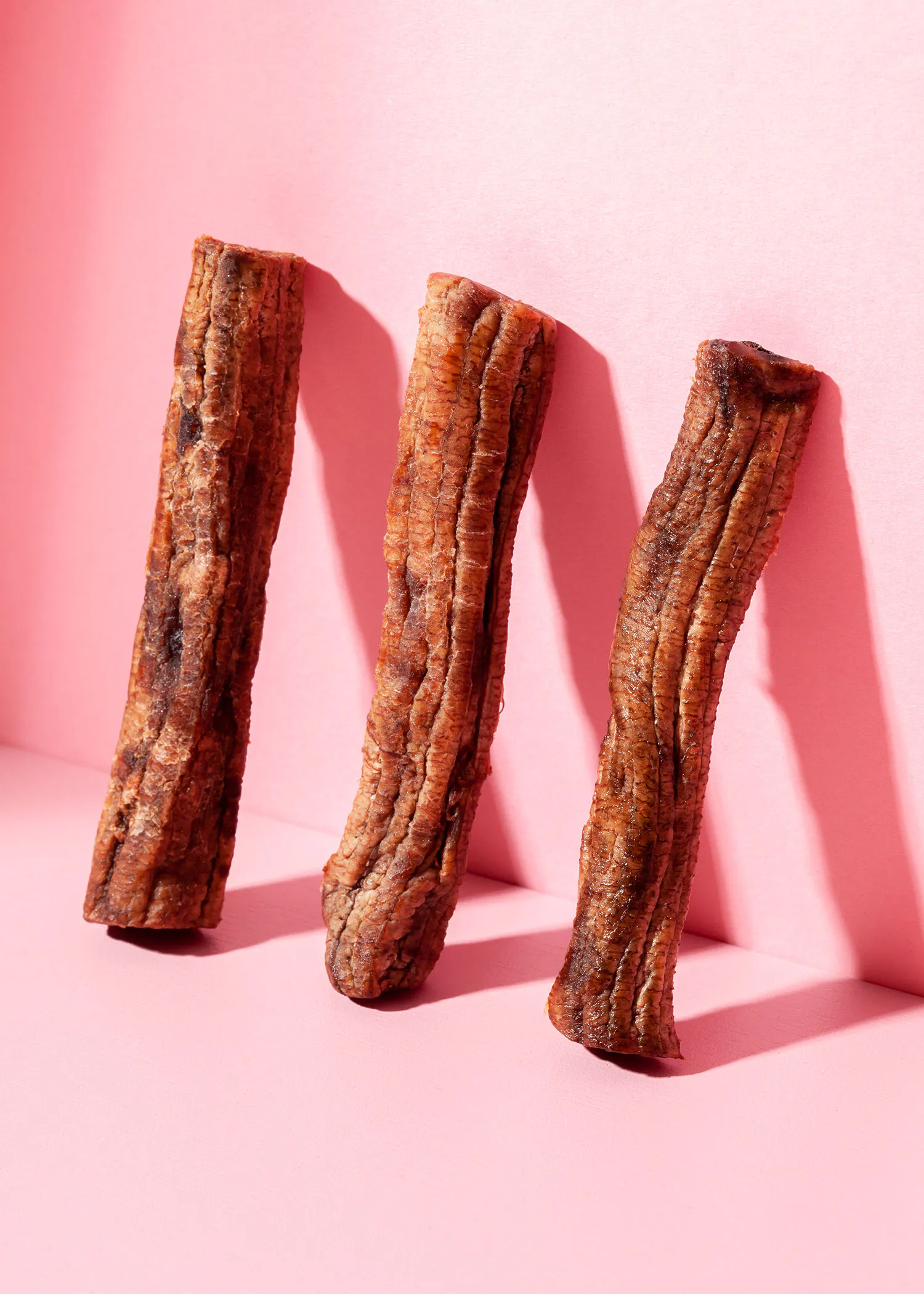 trois bâtonnets de bananes séchées sur fond rose