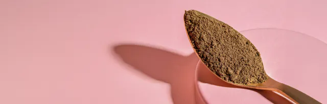 ein goldener löffel gefüllt mit braunem pulver liegt auf einem runden rosa podest vor einem rosa hintergrund.