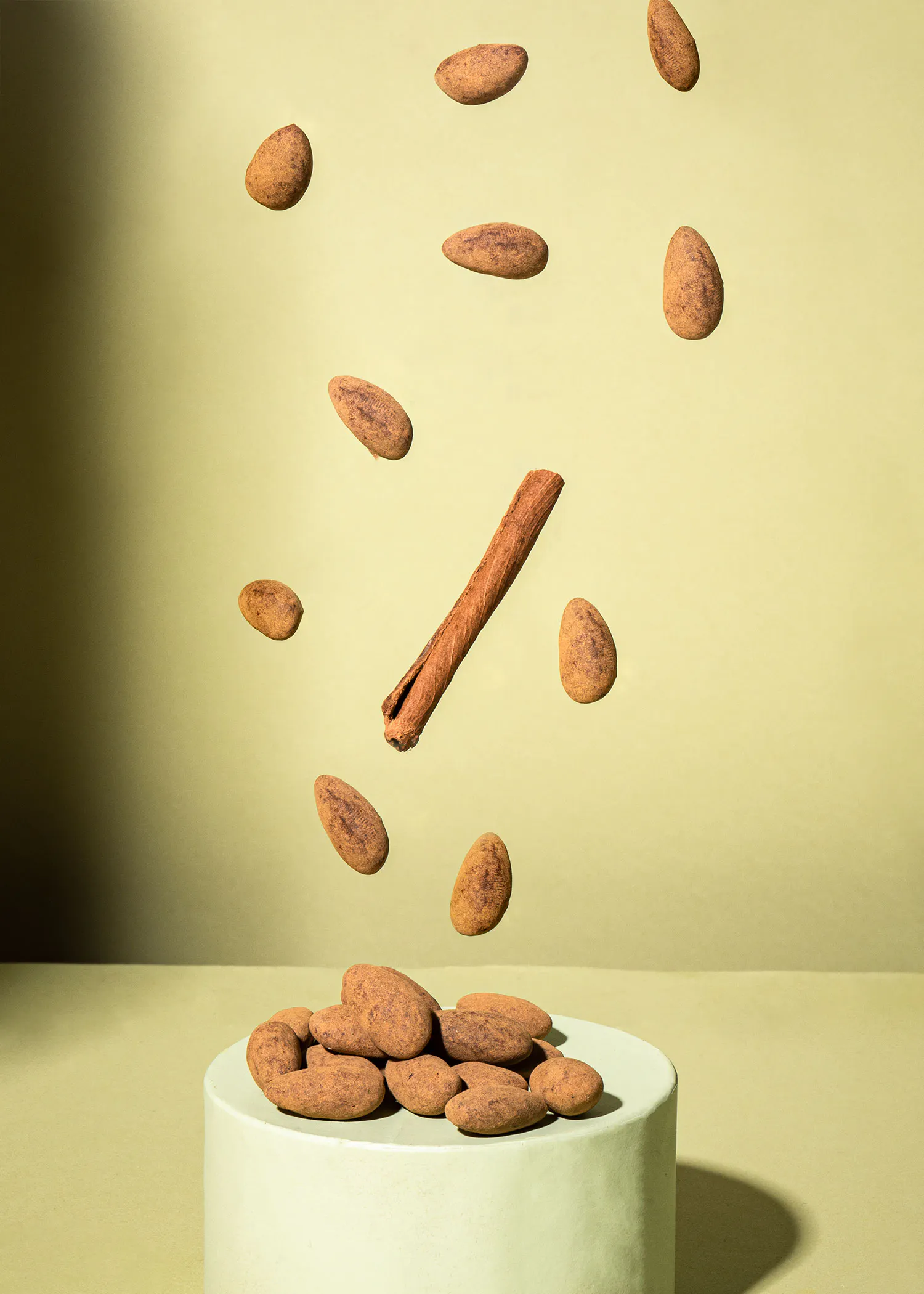 Mandeln und Zimtstangen fallen auf einen weißen Sockel