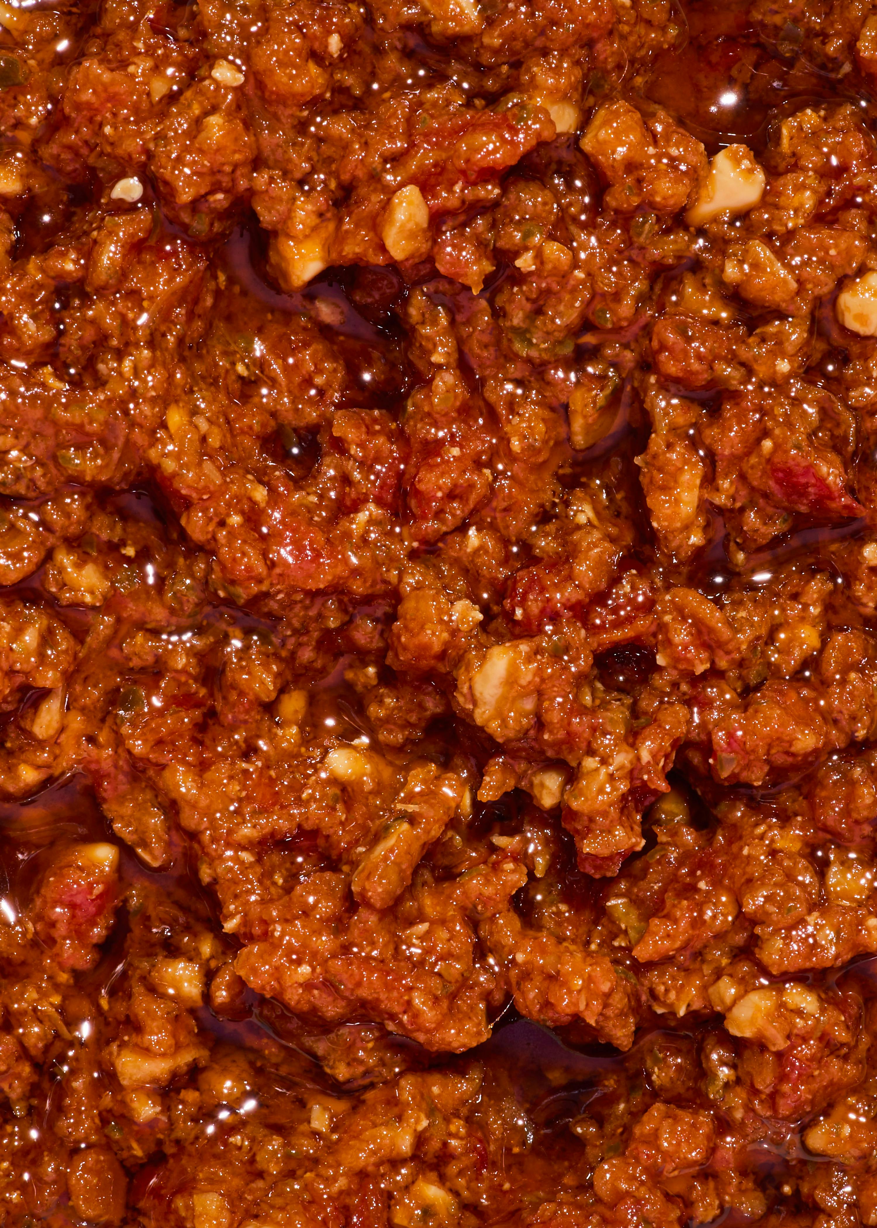 primo piano di una salsa rossa densa e granulosa con pezzi di ingredienti e una superficie lucida.