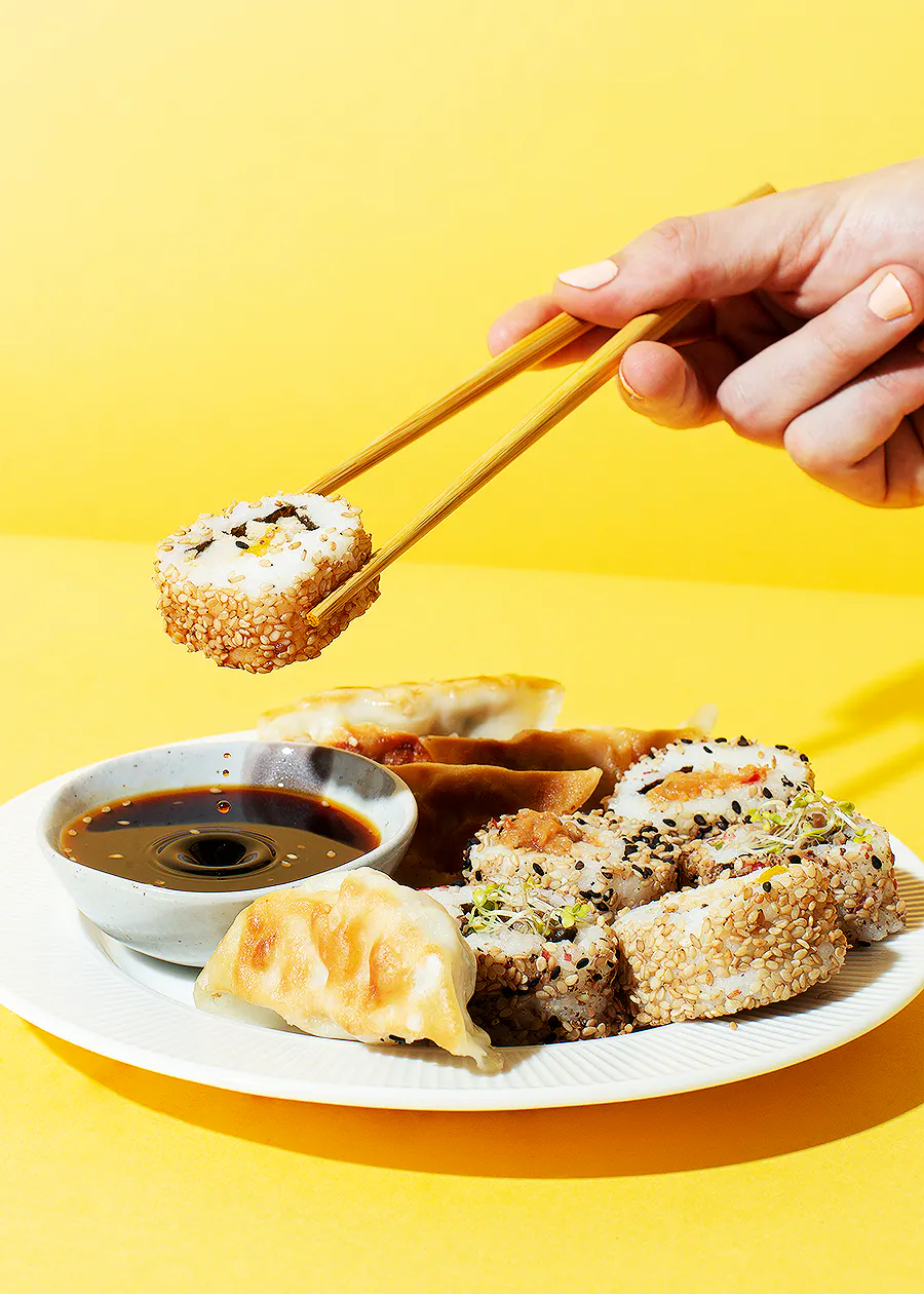 una persona mangia sushi con le bacchette su un piatto bianco