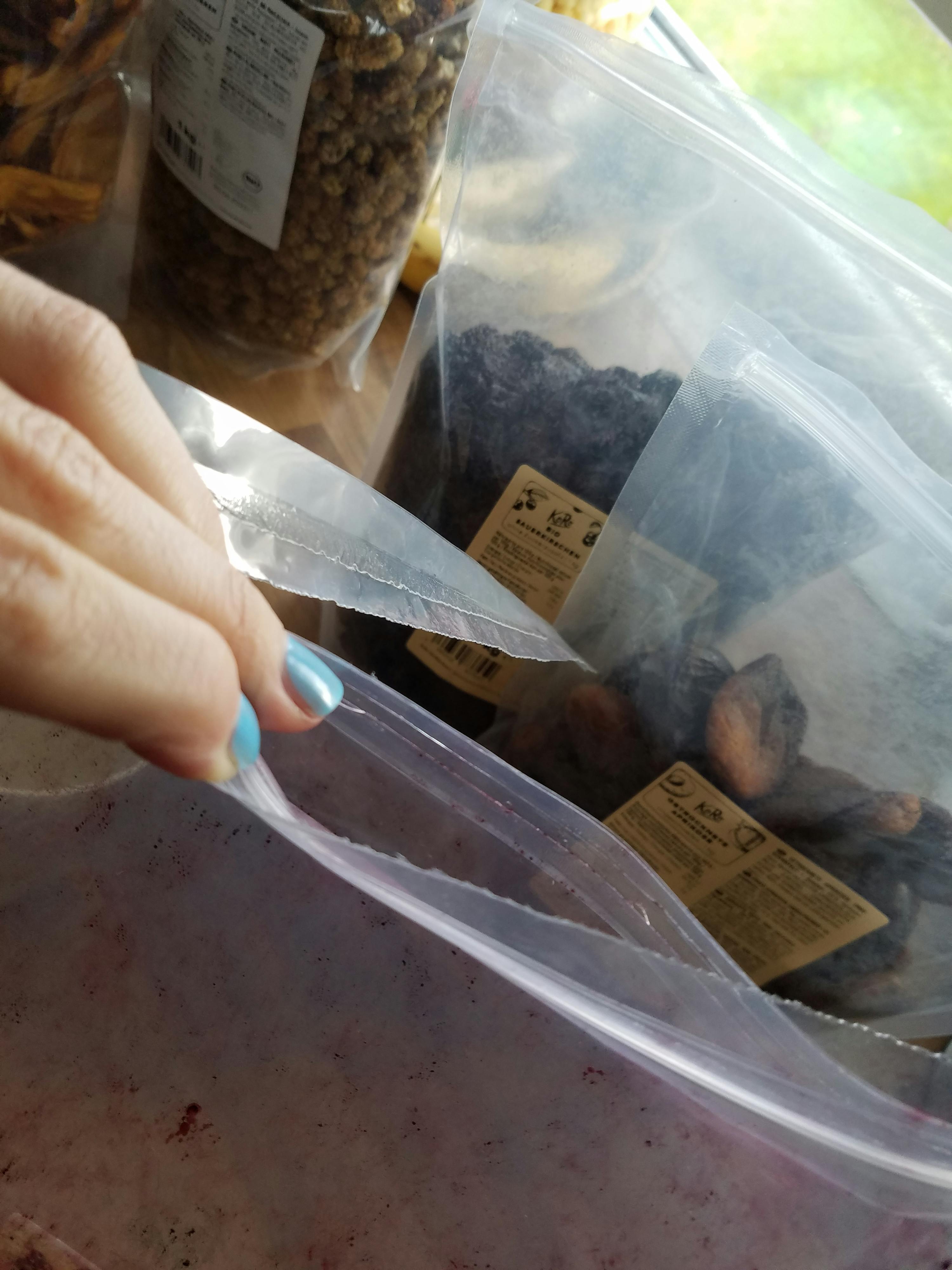 une main avec des ongles bleus tient un sac en plastique