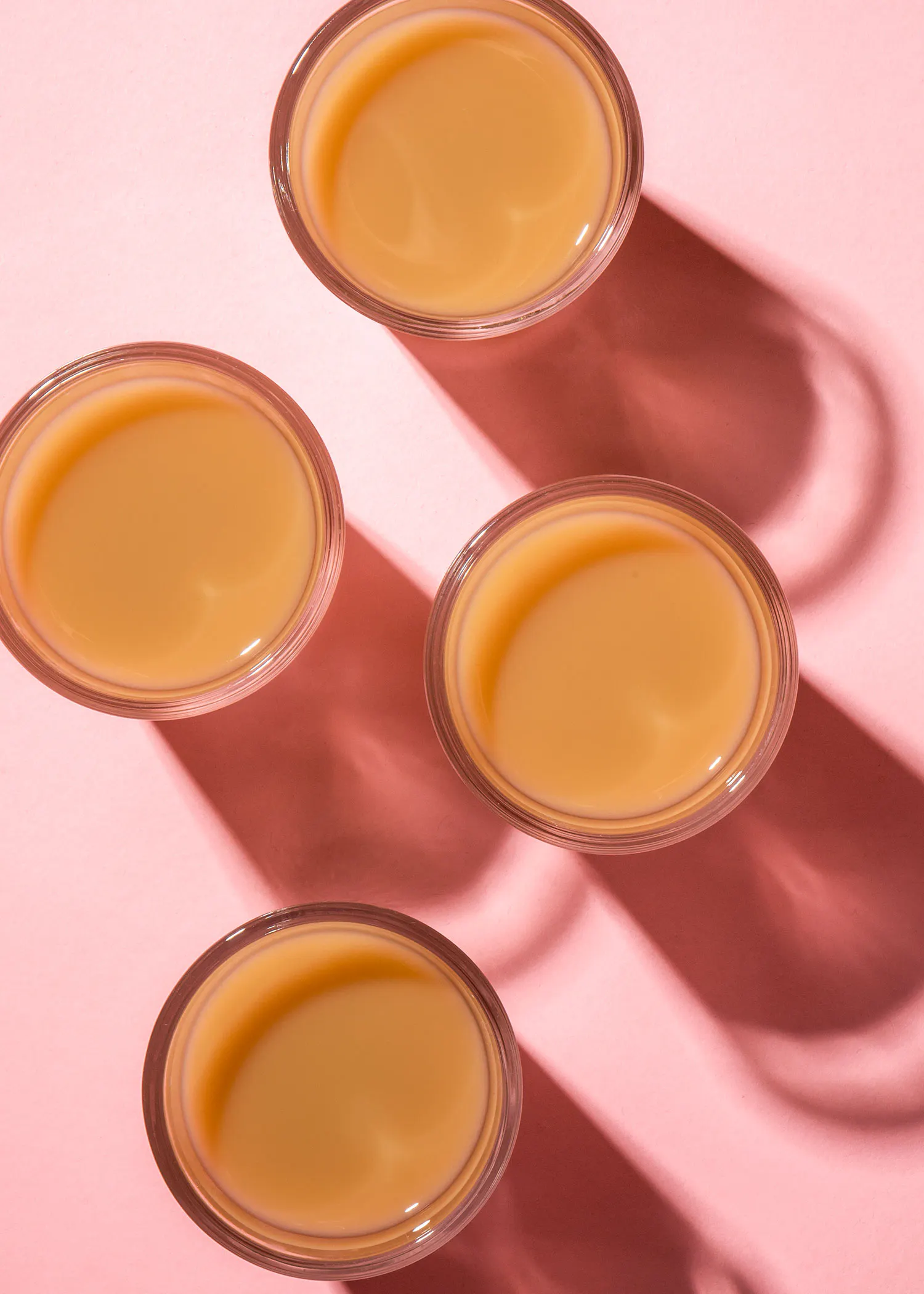 quatre verres remplis d' un liquide jaune sur fond rose