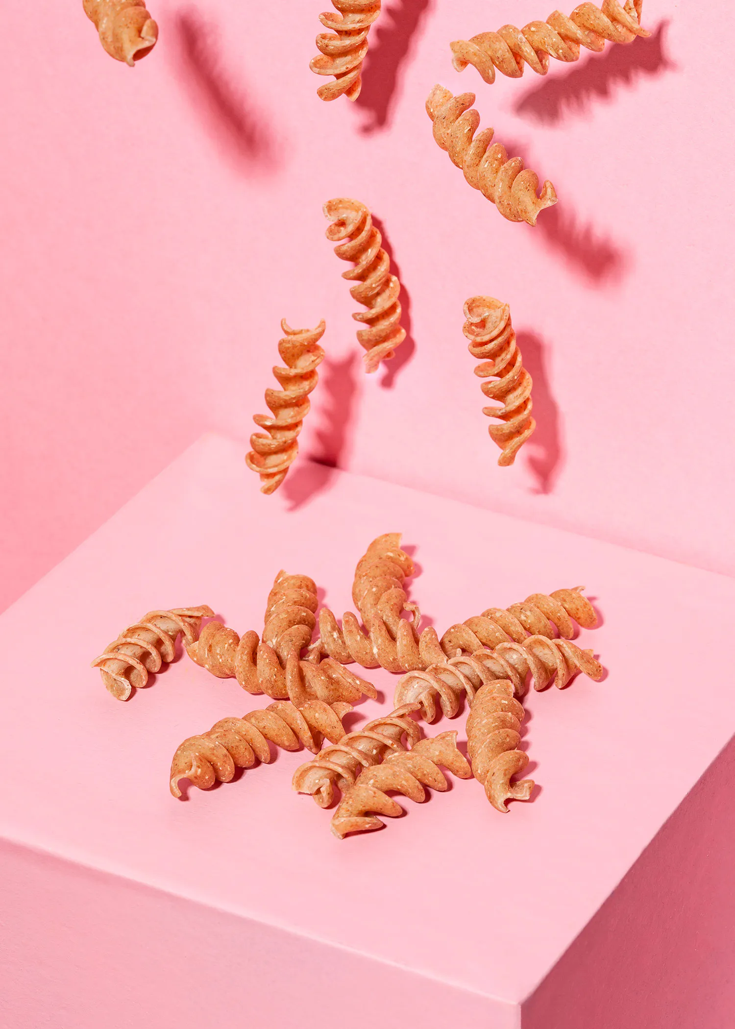 a bunch of pasta is falling on a pink surface