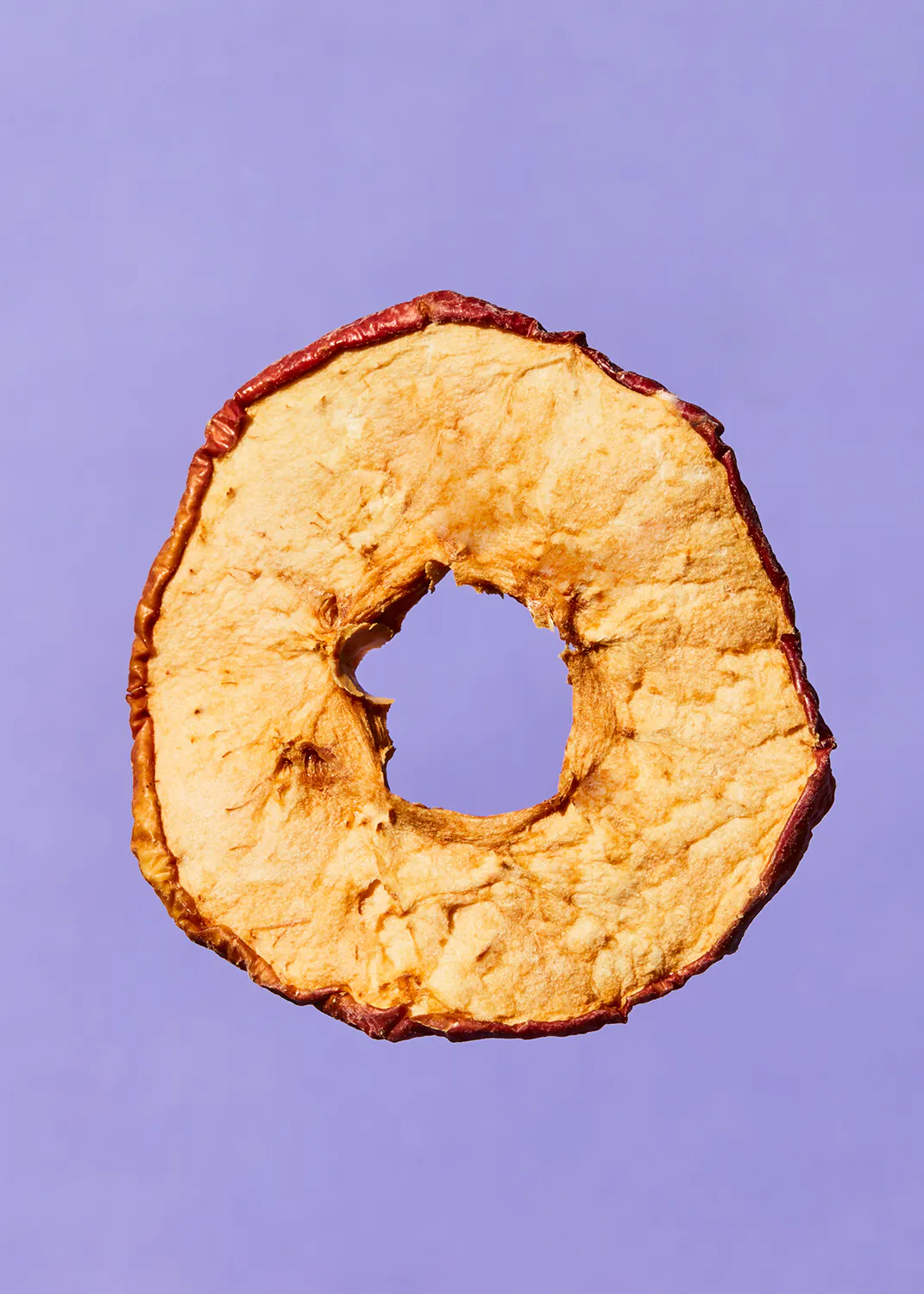 a slice of apple with a hole in the middle on a purple background