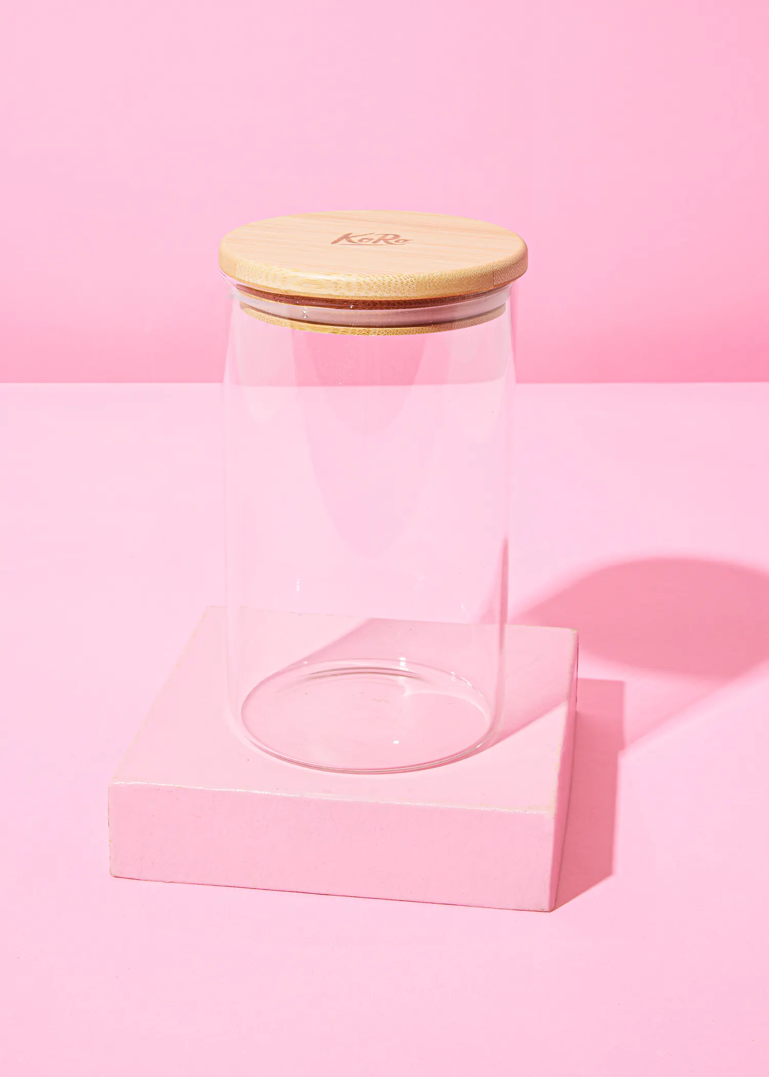 ein Glasgefäß mit einem Holzdeckel steht auf einem rosa Ständer