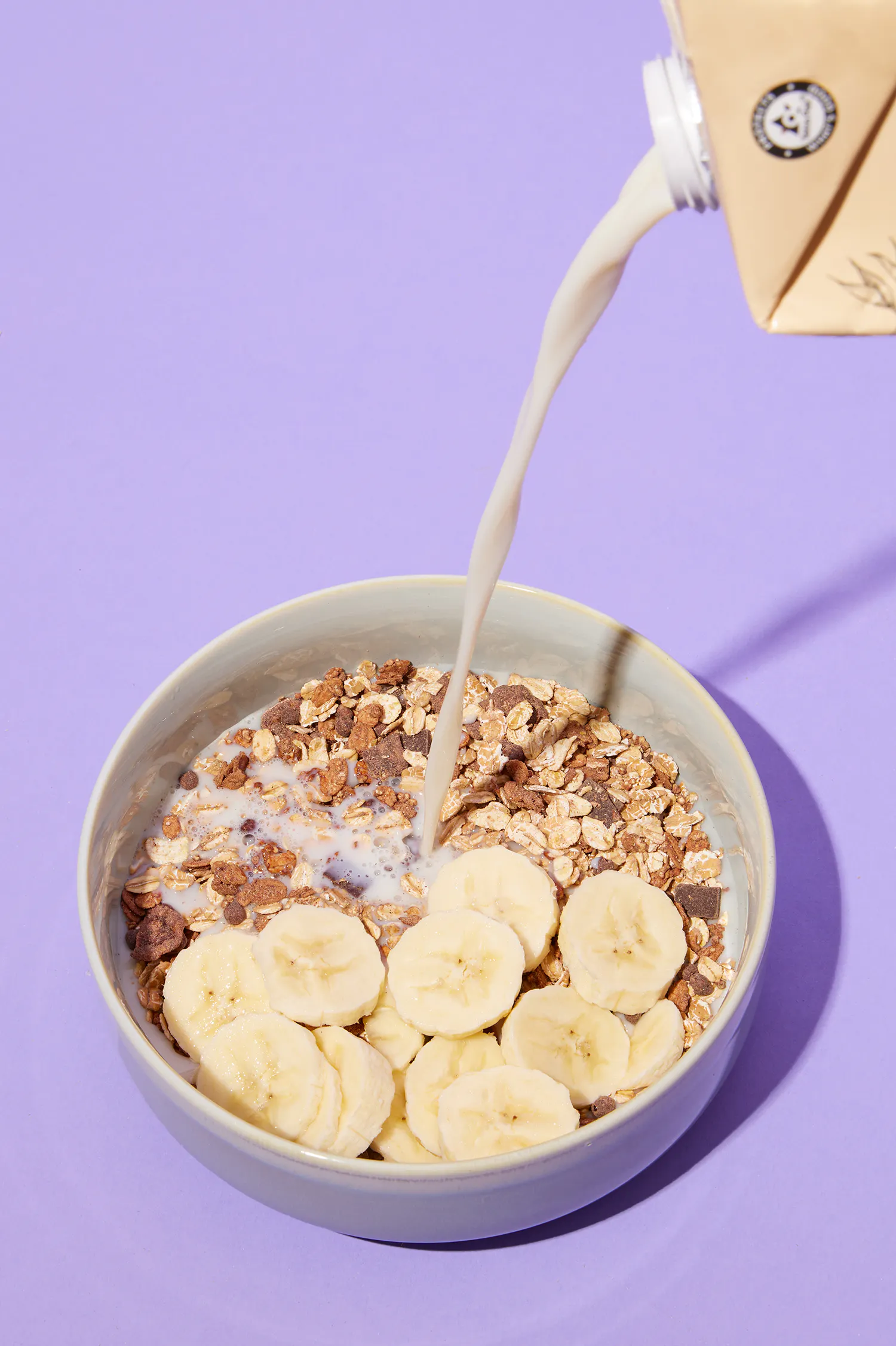 milk is being poured into a bowl of granola and bananas