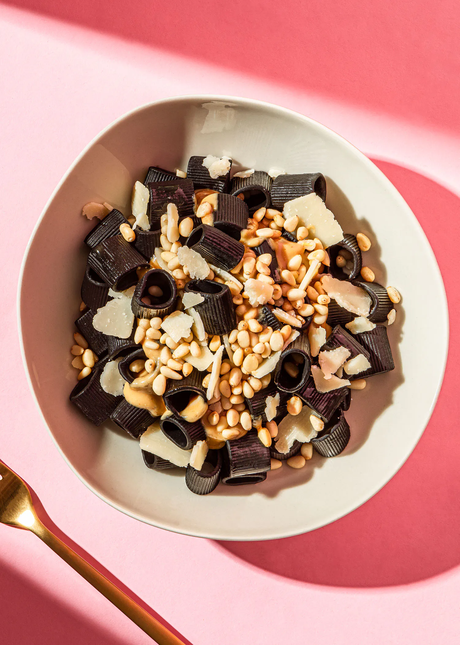 un bol blanc rempli de pâtes noires , de noix de pin et de parmesan