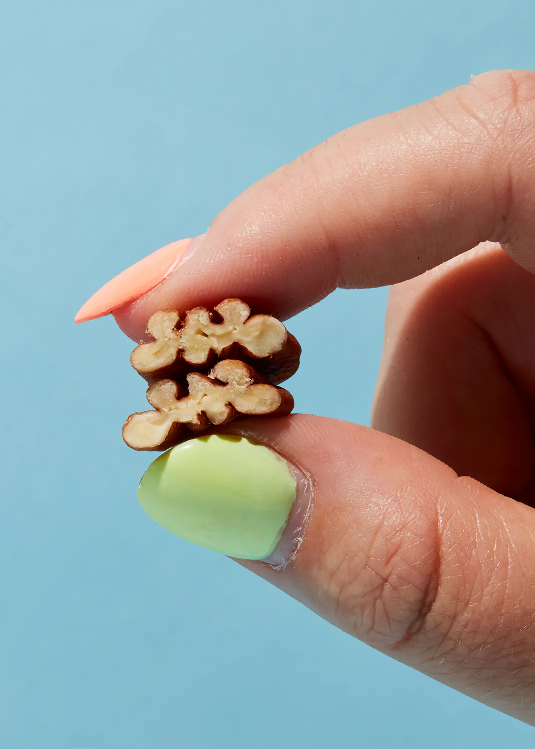 a person with green nails holds a walnut in their hand