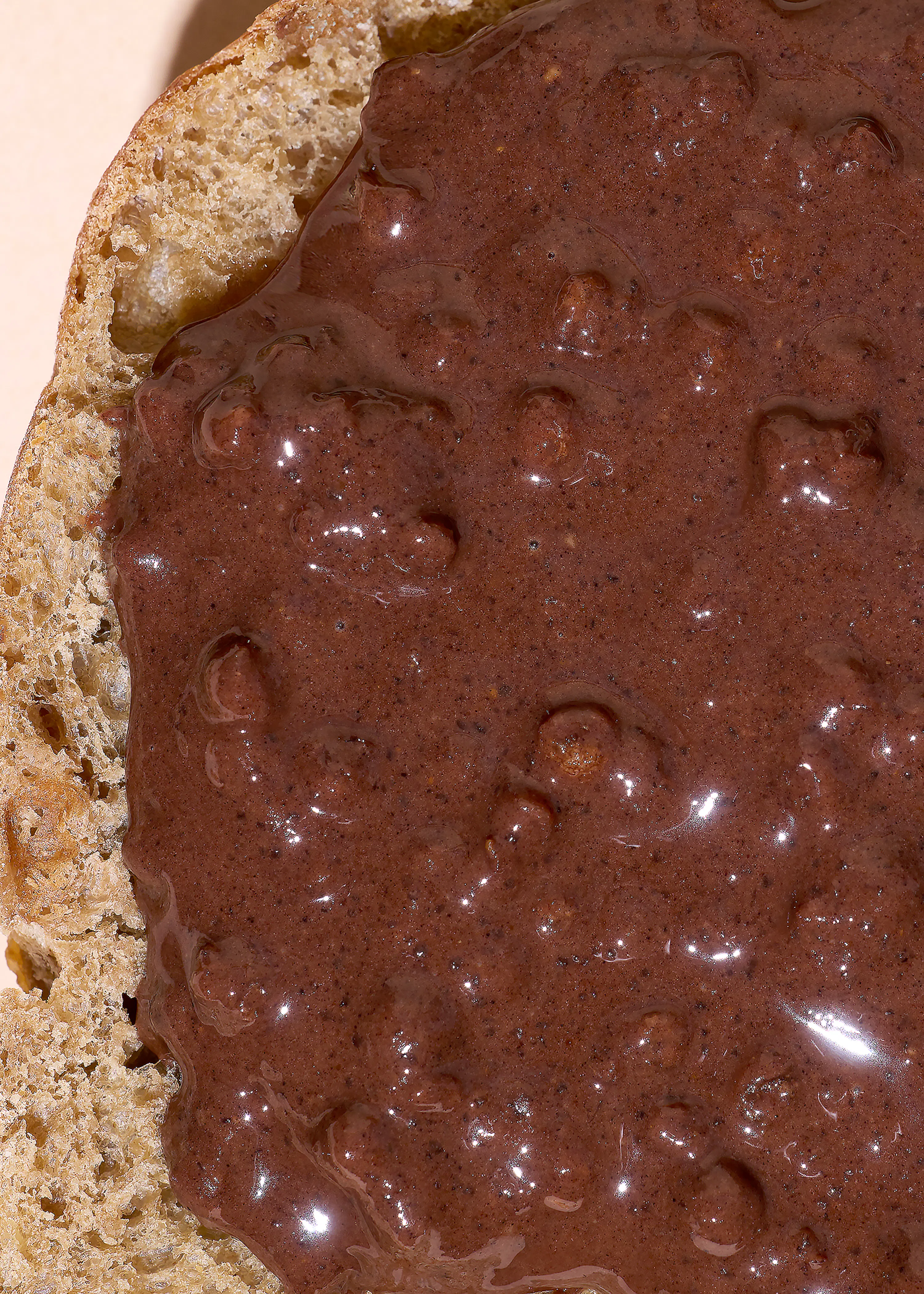 ein stück brot mit dickem, glänzendem, dunkelbraunem aufstrich, der kleine stücke enthält.