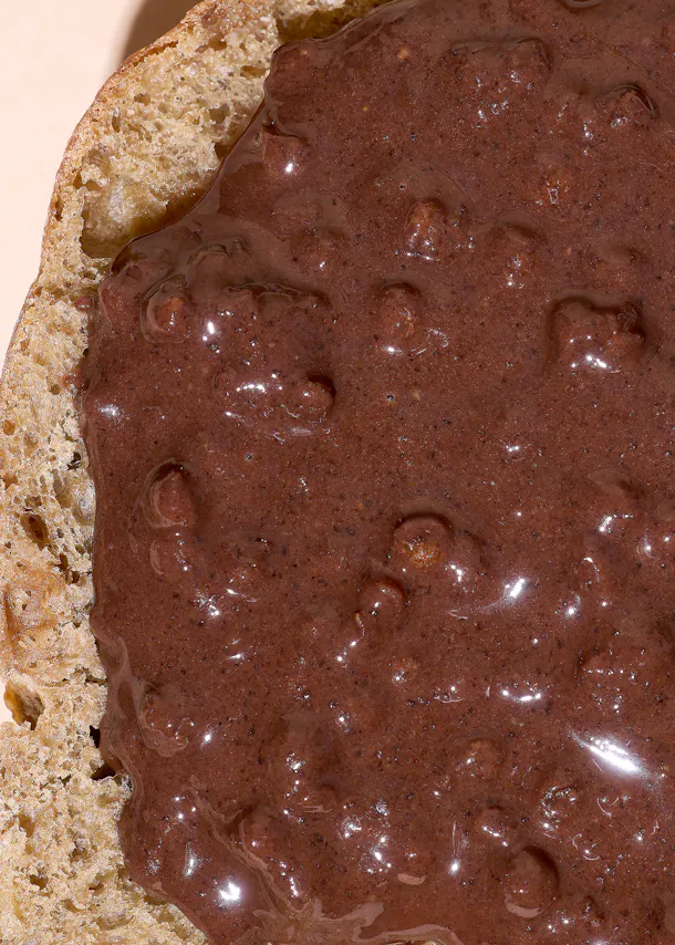 une tranche de pain recouverte d'une pâte à tartiner brune épaisse et brillante.
