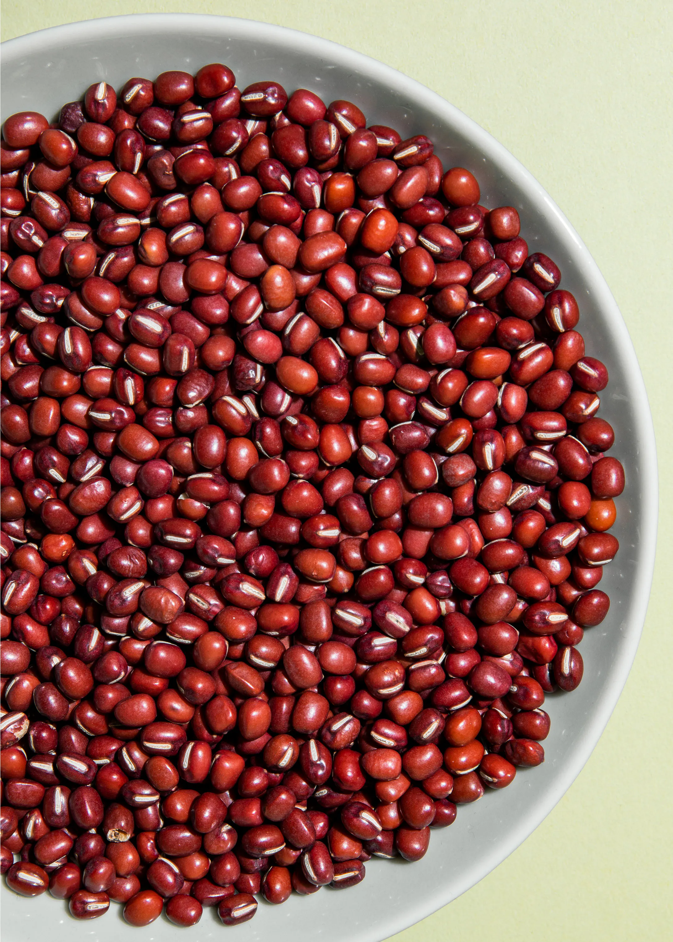 a white bowl filled with red beans has a yellow background