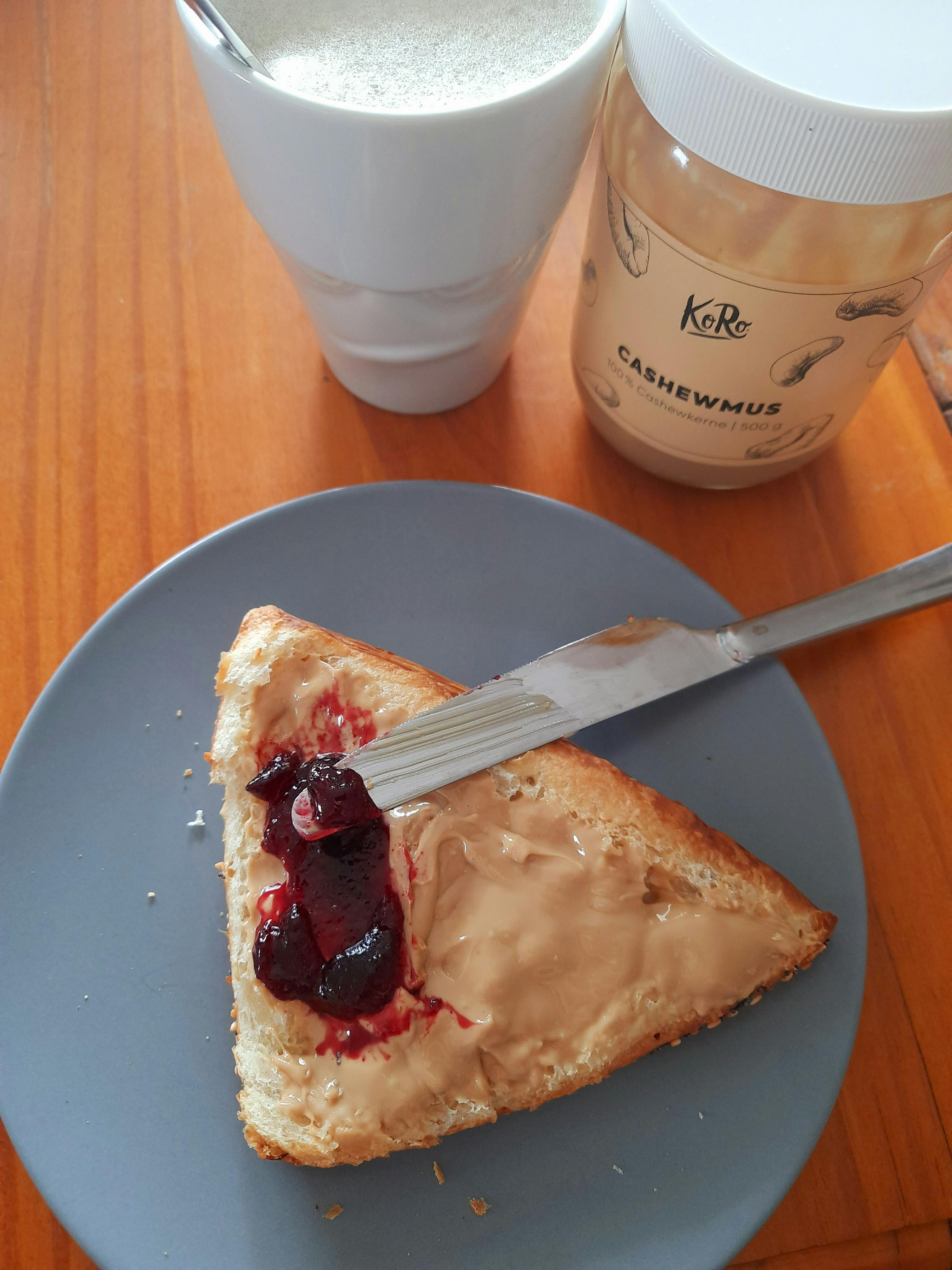 a slice of bread with peanut butter and jelly next to a jar of cashewmus