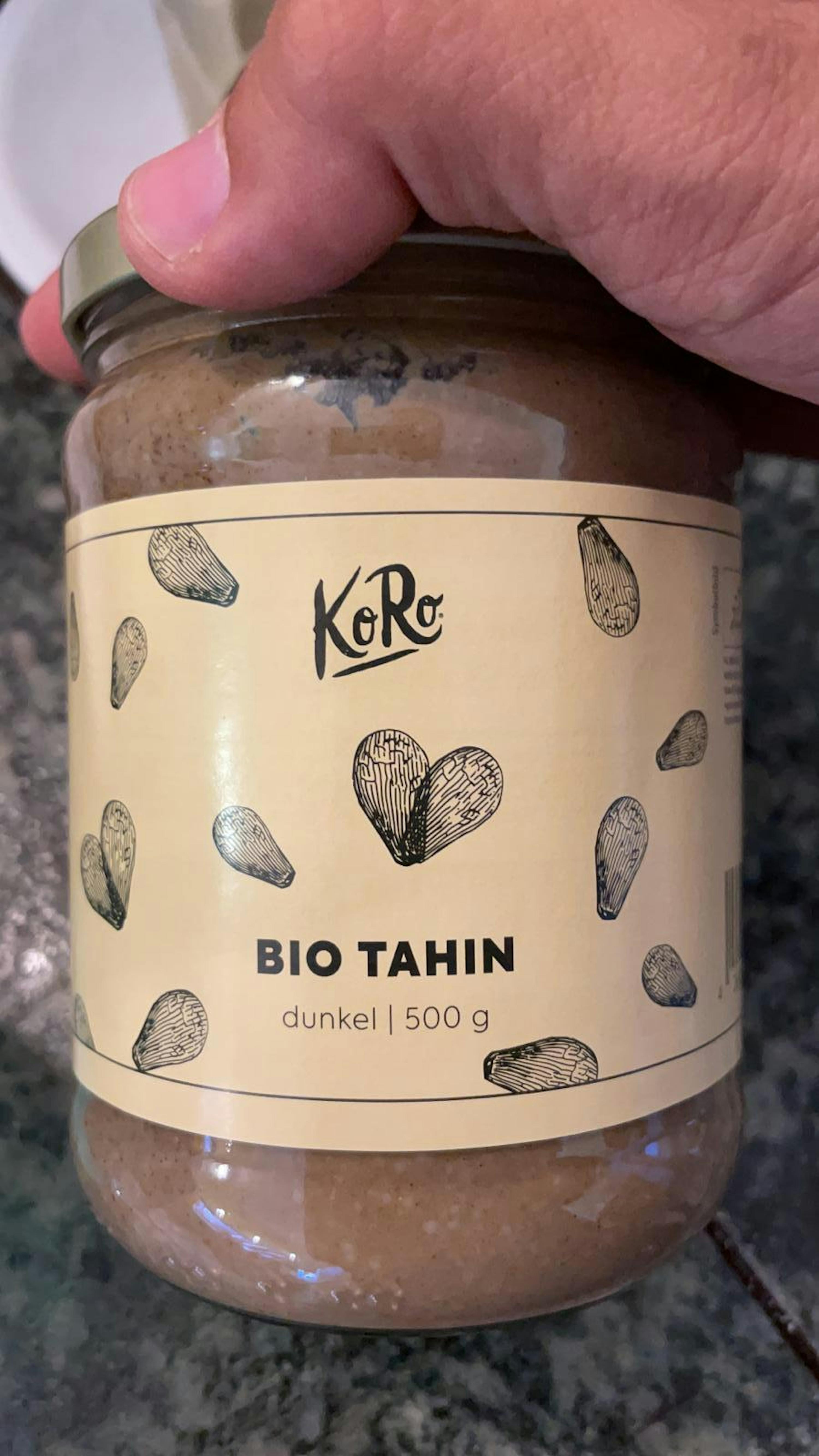 une personne tient un pot de tahin bio dans sa main