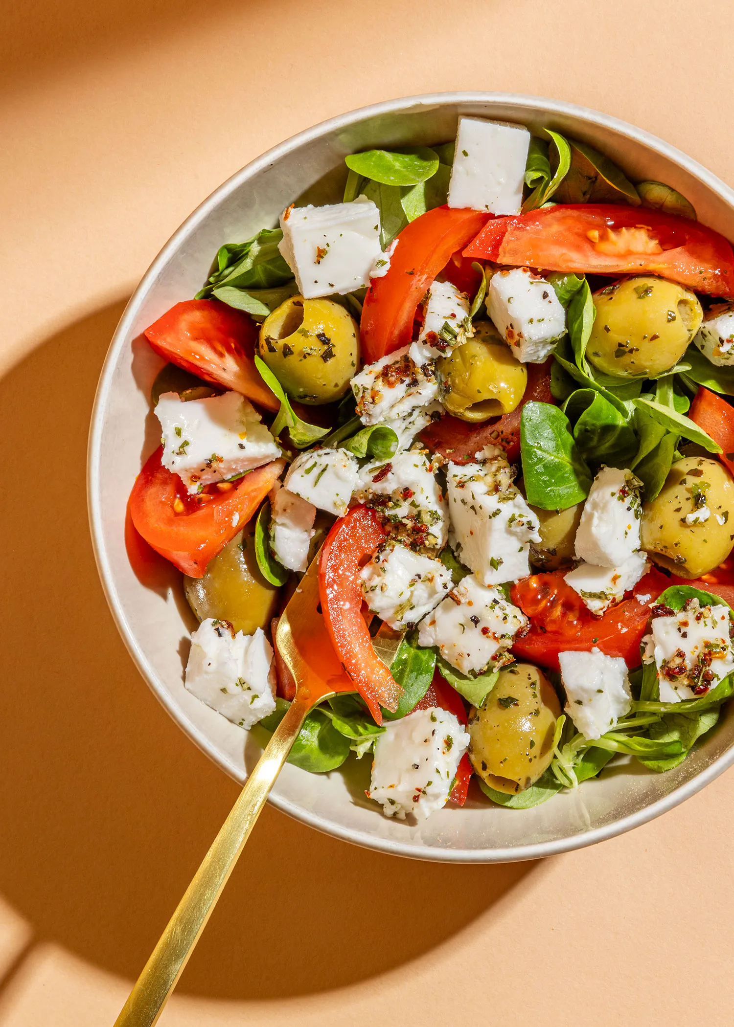 un bol de salade avec des tomates des olives et du fromage avec une fourchette