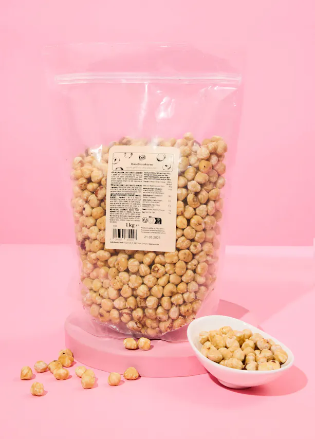 un sac de noisettes est assis sur une surface rose à côté d' un bol de noisettes