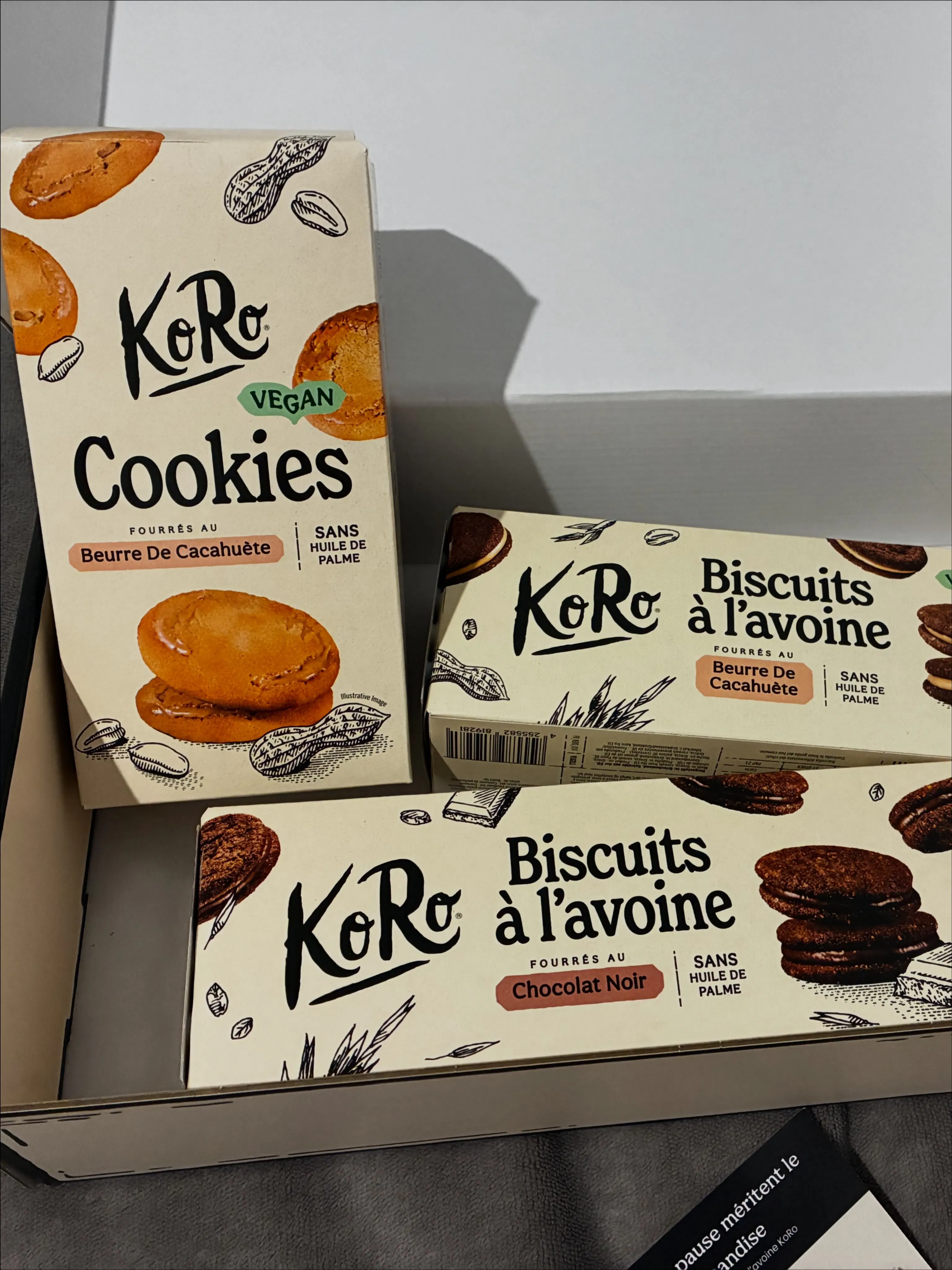three boxes of koro brand vegan cookies and oat biscuits with peanut butter and dark chocolate fillings displayed in a box.