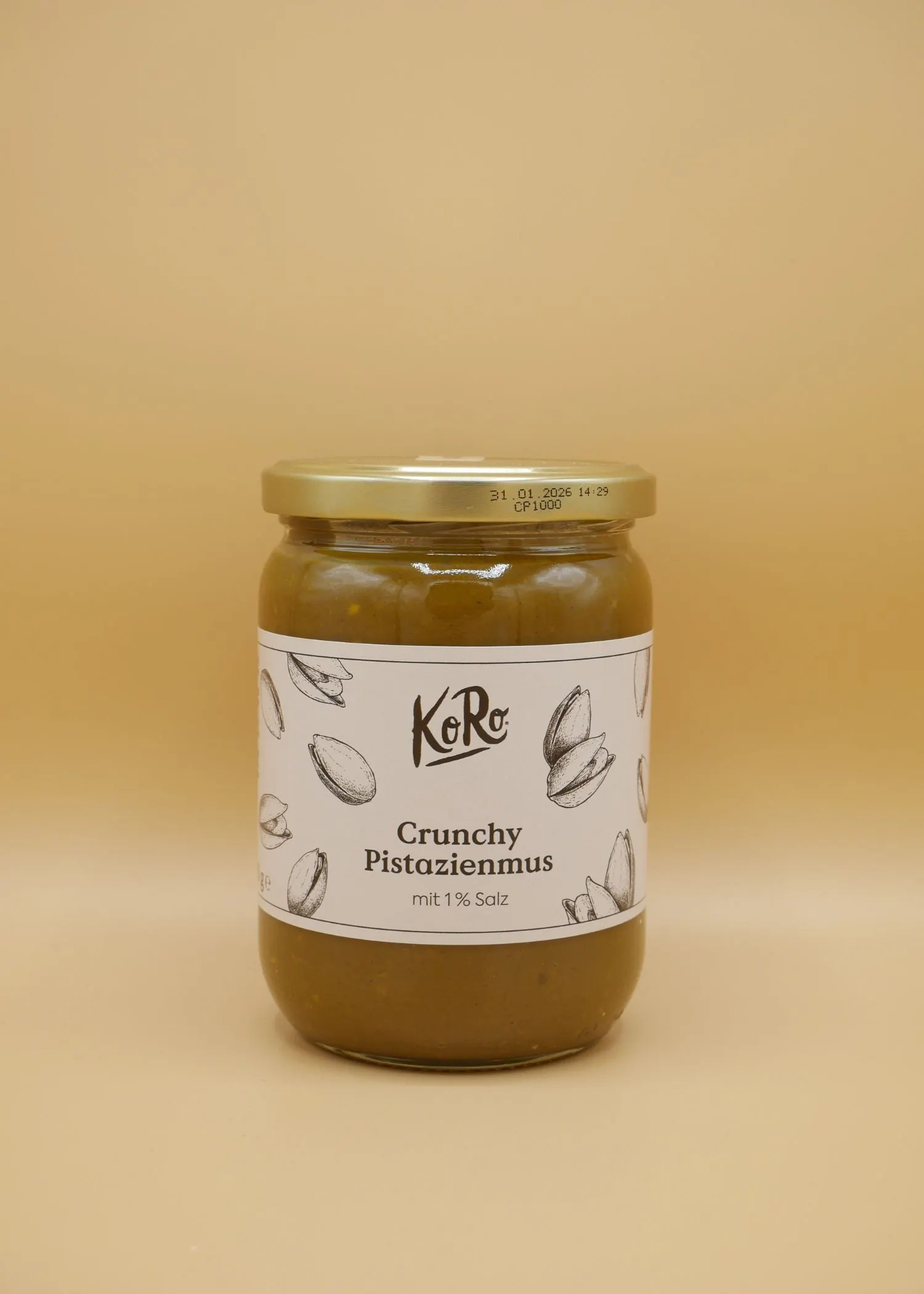 a jar of koro crunchy pistachio butter with 1% salt, a gold lid, and a white label with pistachio illustrations is displayed against a beige background.