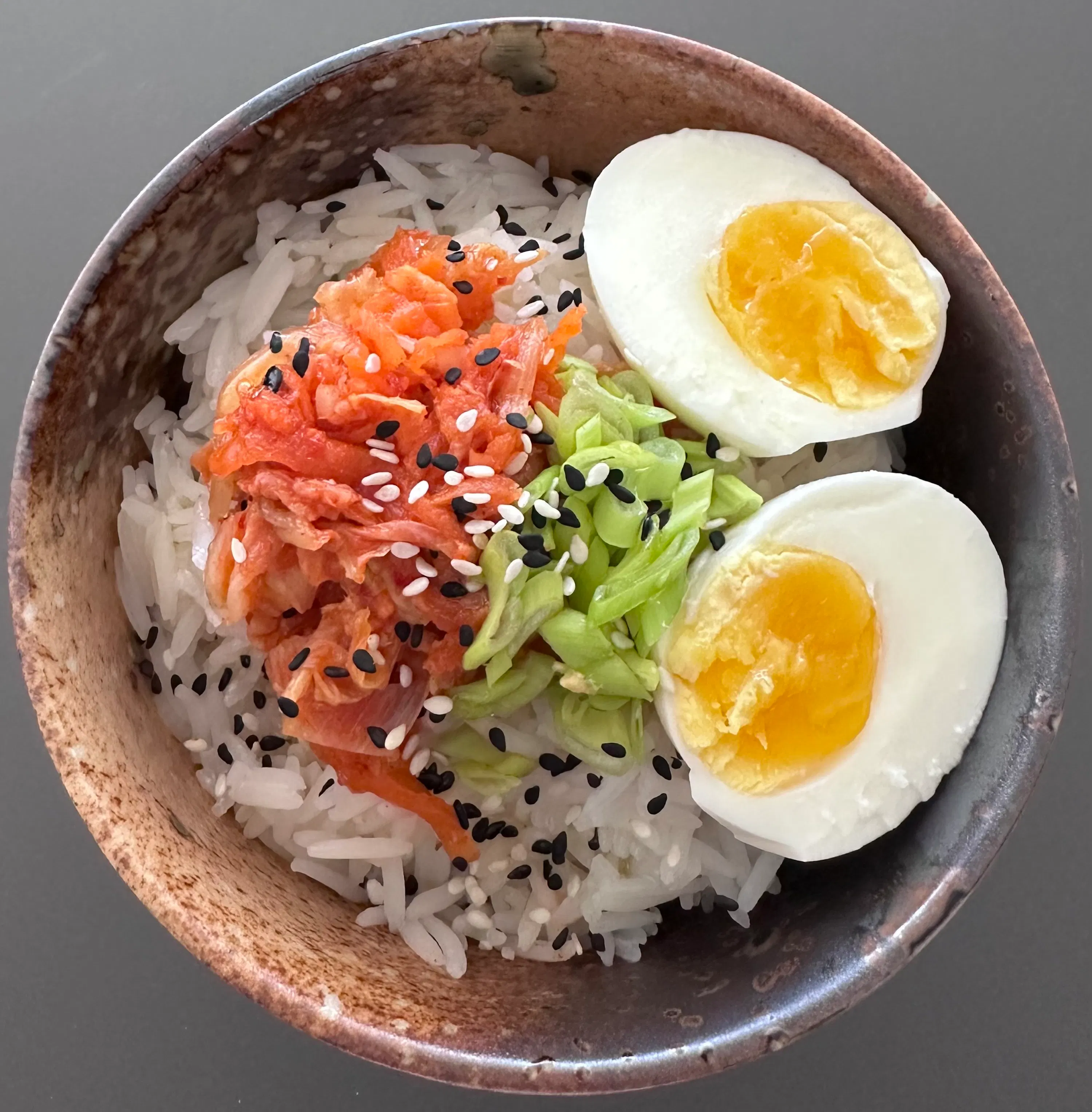 eine schale mit reis, kimchi, gehackten grünen zwiebeln, zwei halben hartgekochten eiern und sesamsamen.