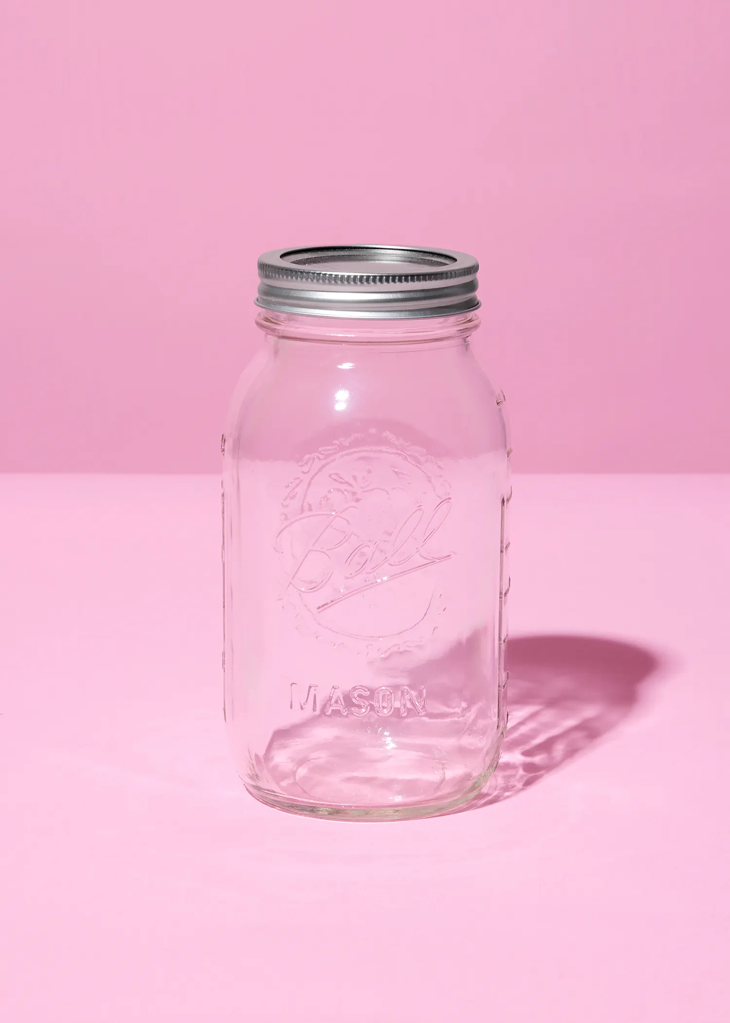 ein klares ball mason glas mit silbernem deckel auf einem pinkfarbenen hintergrund.