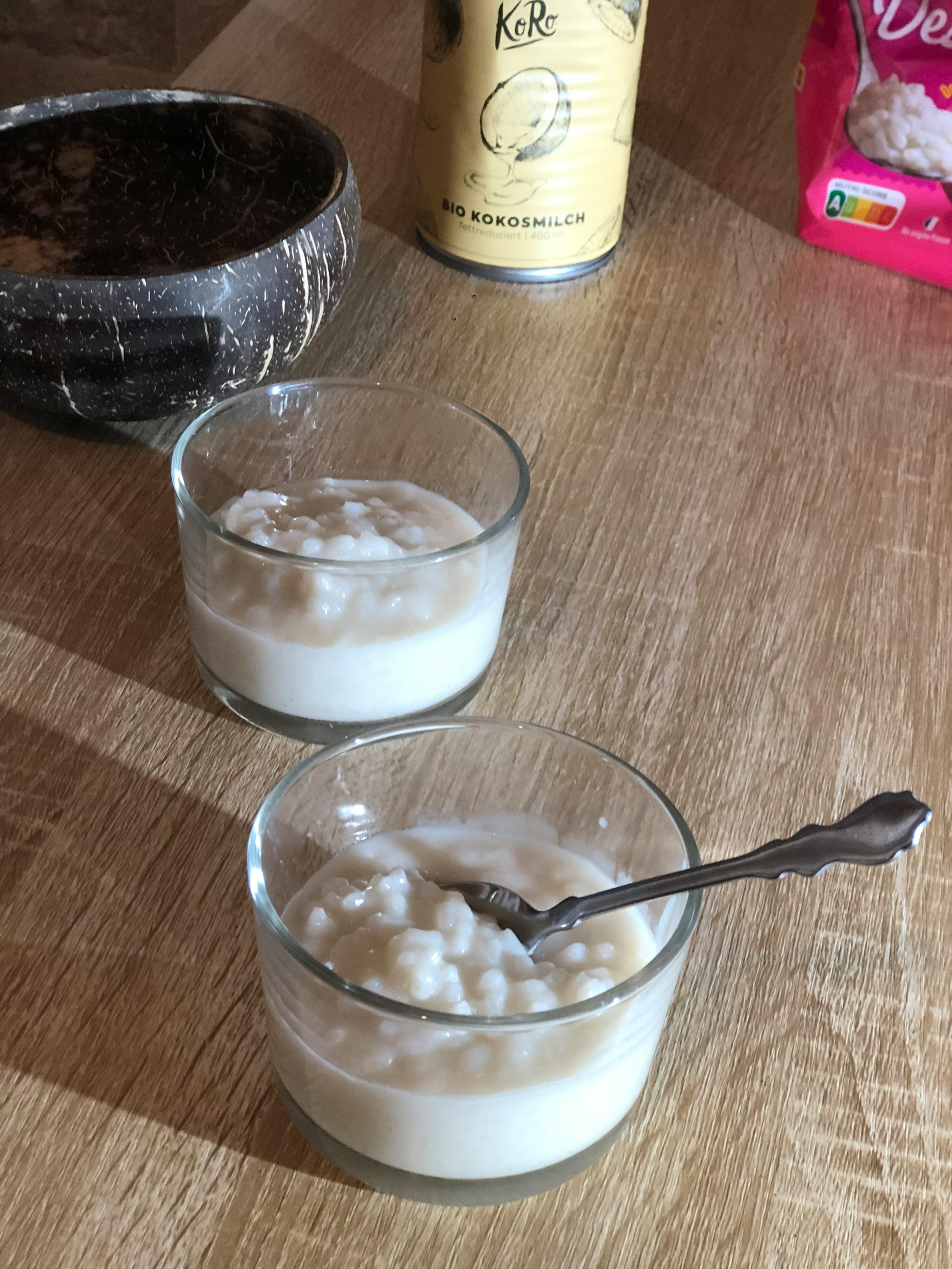 a can of kokosmilch sits on a wooden table next to two bowls of food