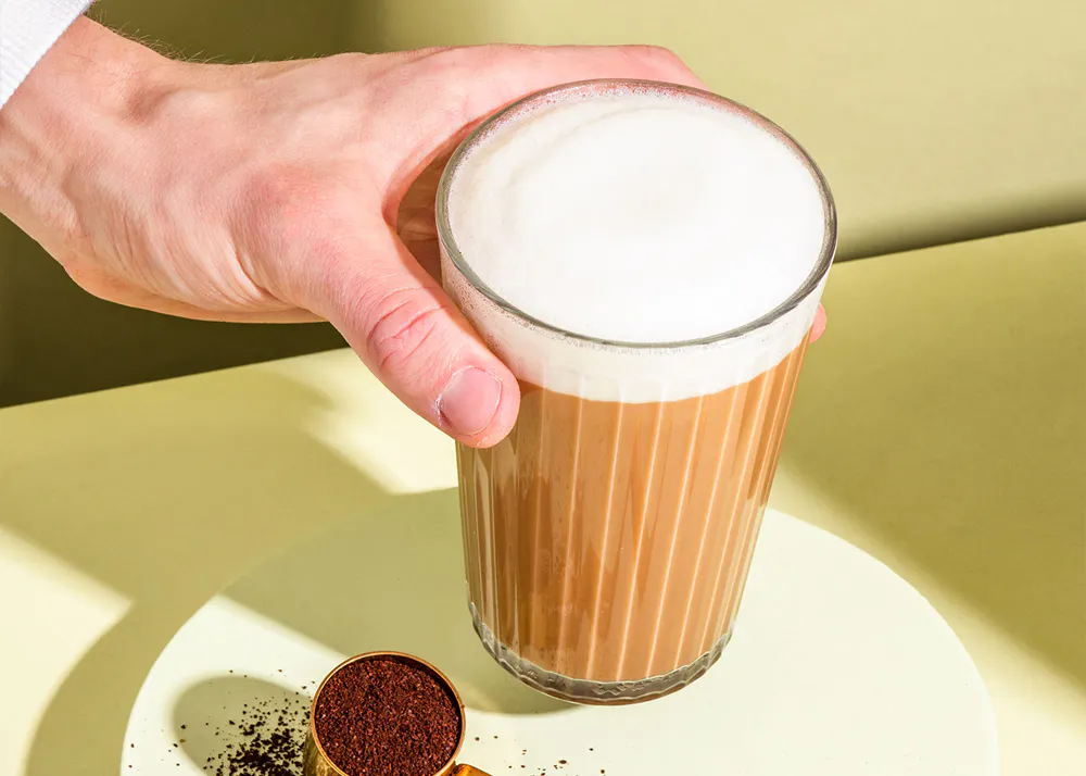 eine Person hält ein Glas Kaffee mit Milchschaum darauf