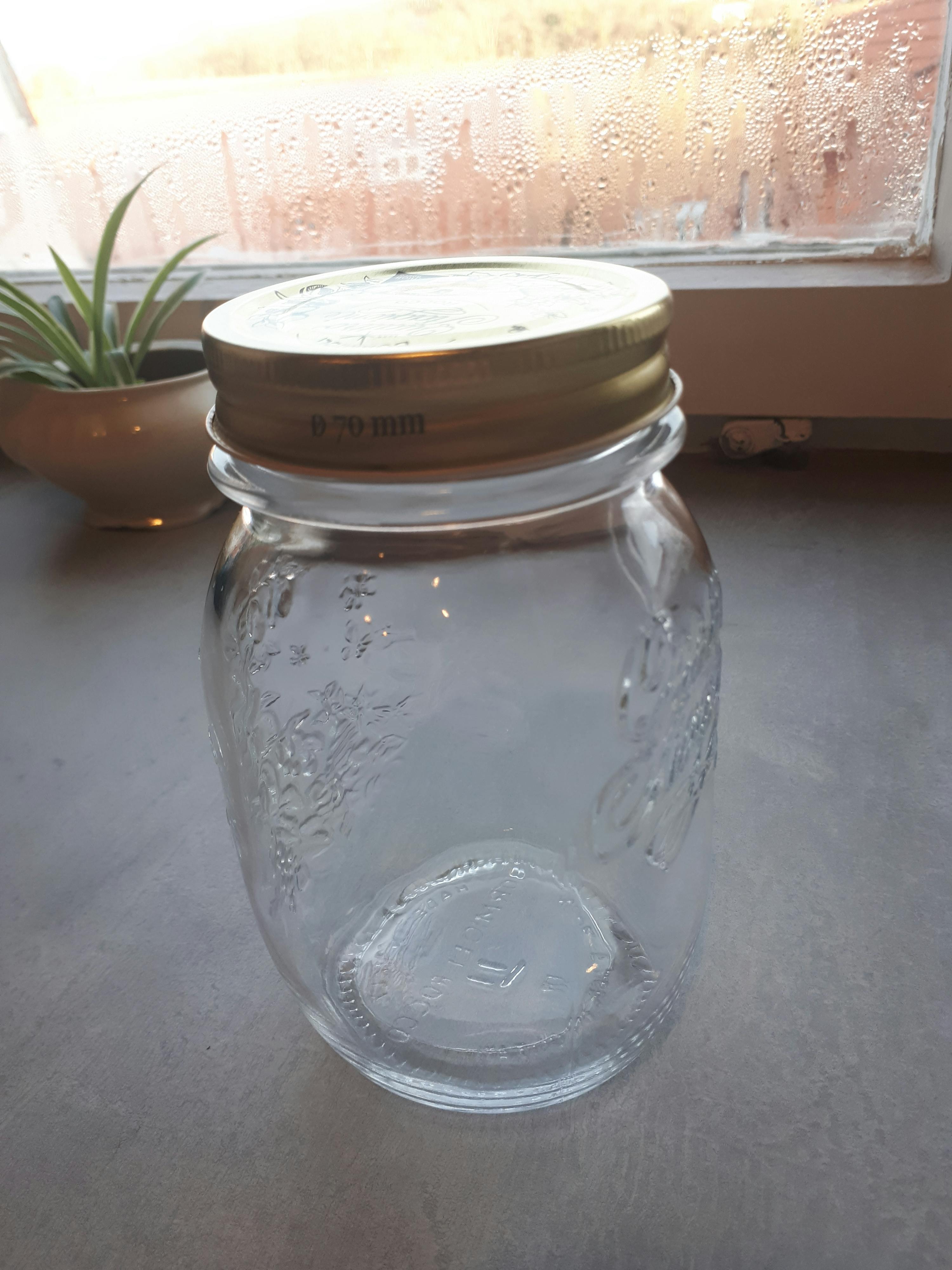 ein Glasgefäß mit einem goldenen Deckel steht auf einem Tisch neben einem Fenster