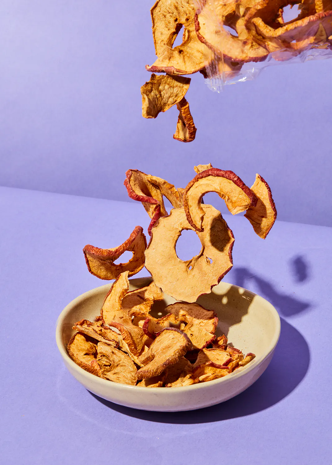 a bowl of dried apple slices on a purple background