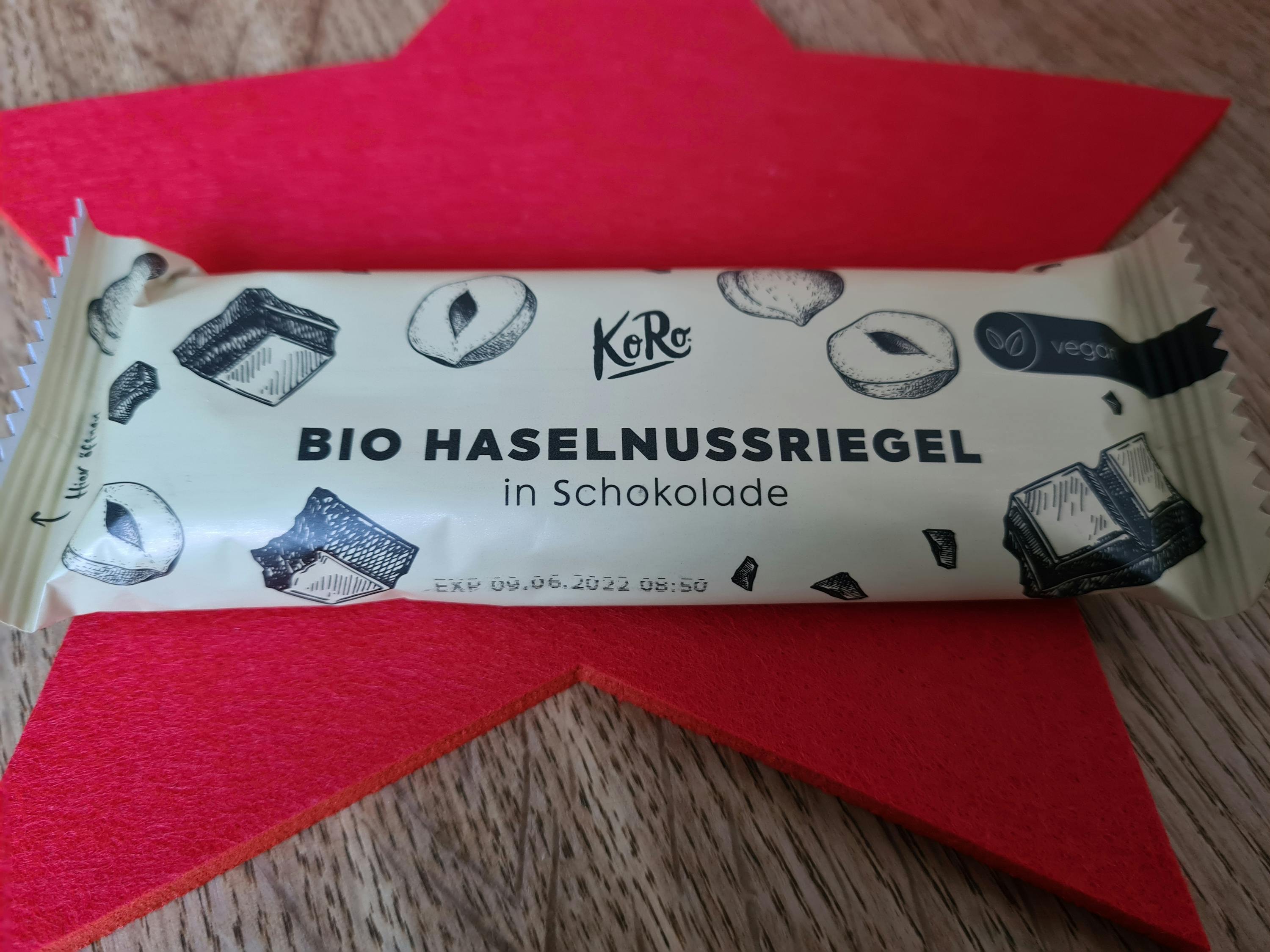 Eine verpackte Bio-Haselnussriegel in Schokolade liegt auf einem roten Stern