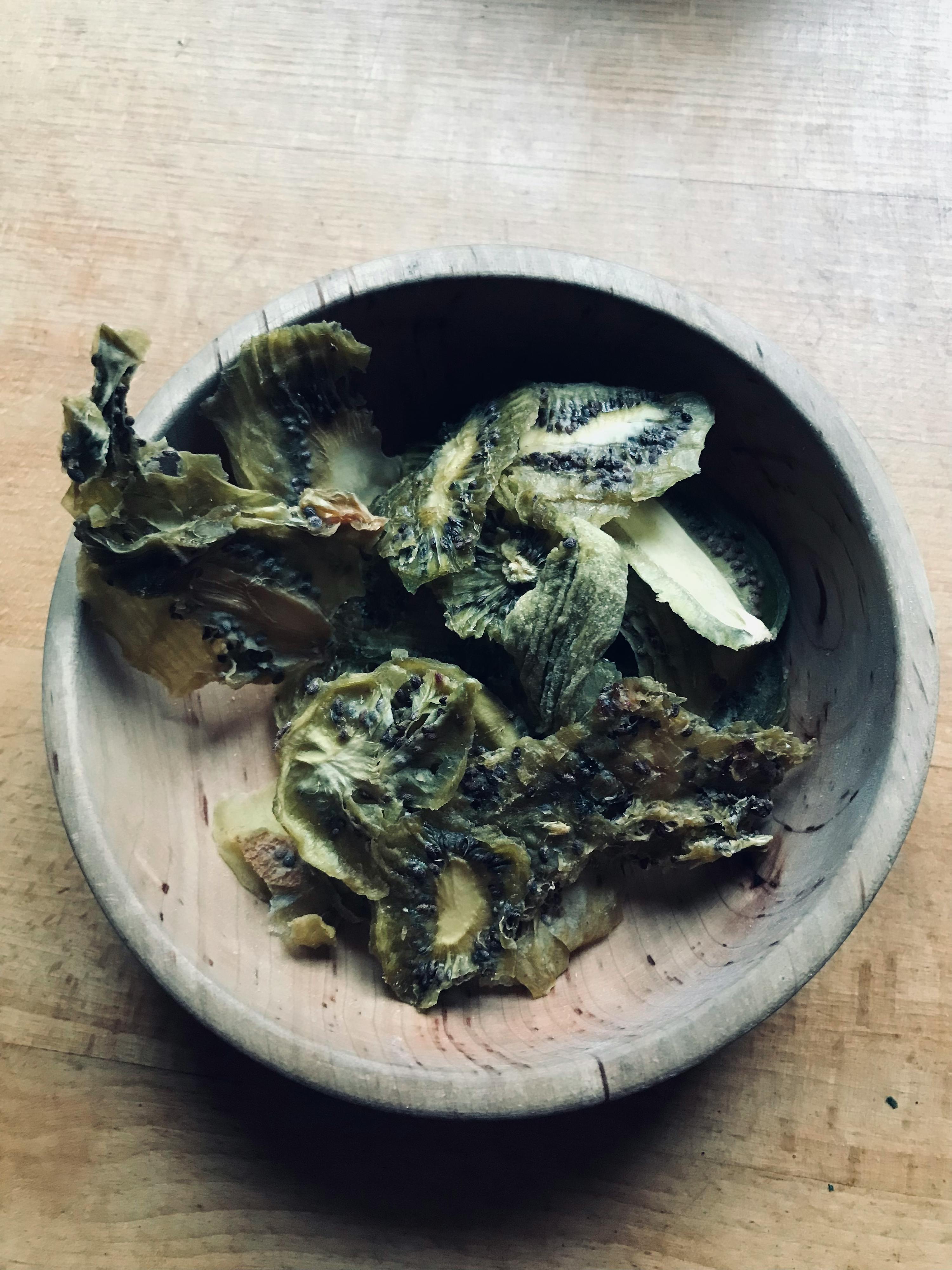 eine hölzerne Schüssel mit getrockneten Kiwis auf einem Holztisch