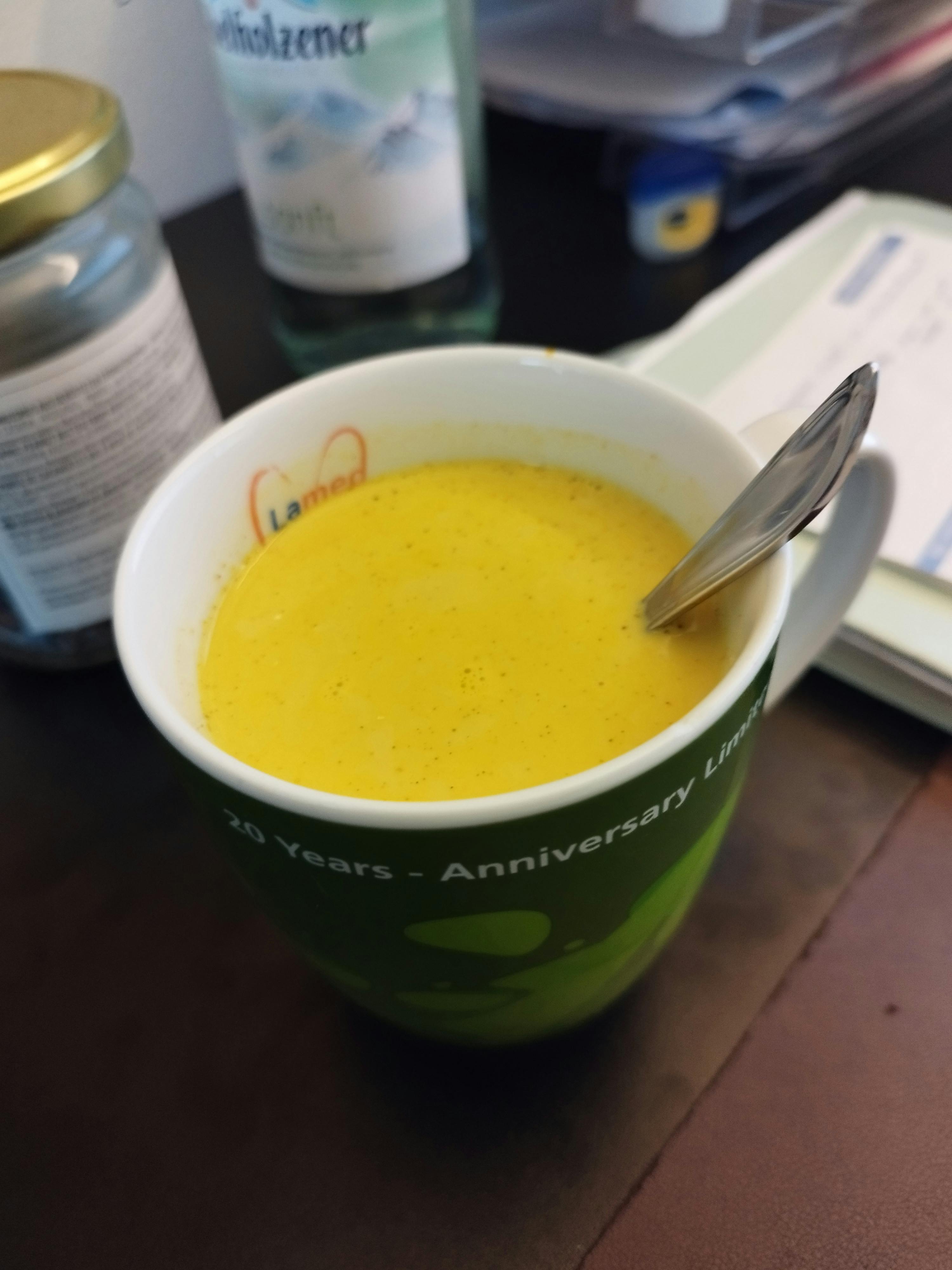 ein grüner becher mit einem gelben getränk und einem löffel darin steht auf einem dunklen tisch.