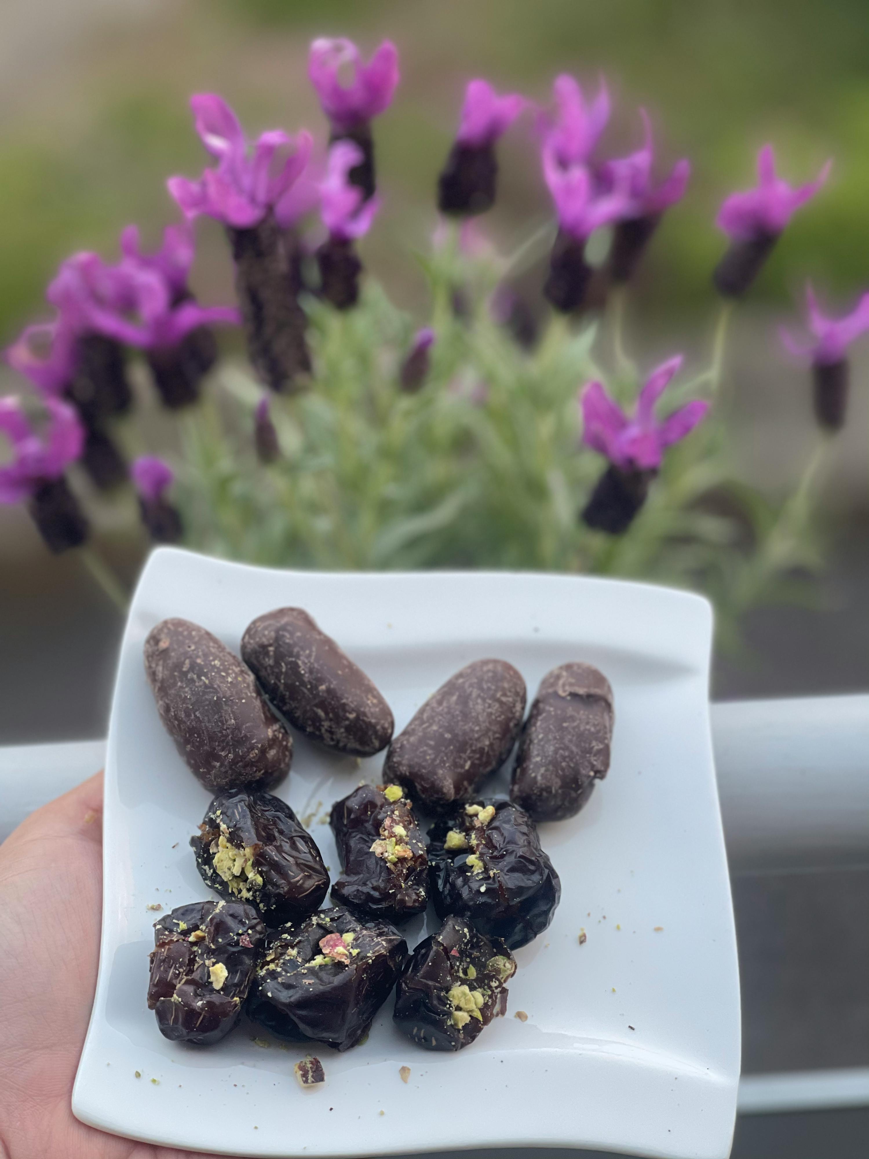 una persona tiene in mano un piatto bianco pieno di frutta secca con fiori viola sullo sfondo